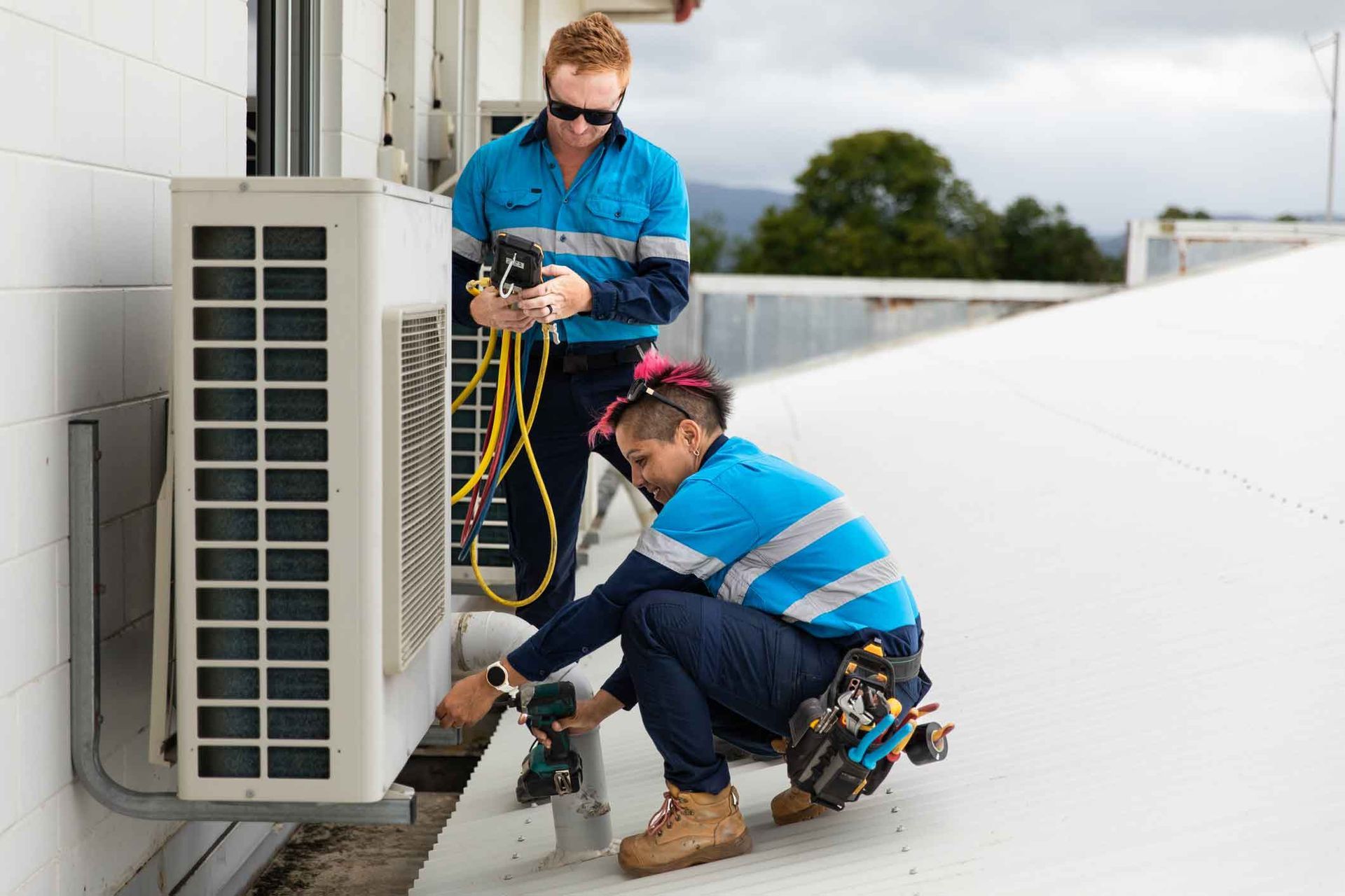 Two men are working on an air conditioner on the roof of a building.
