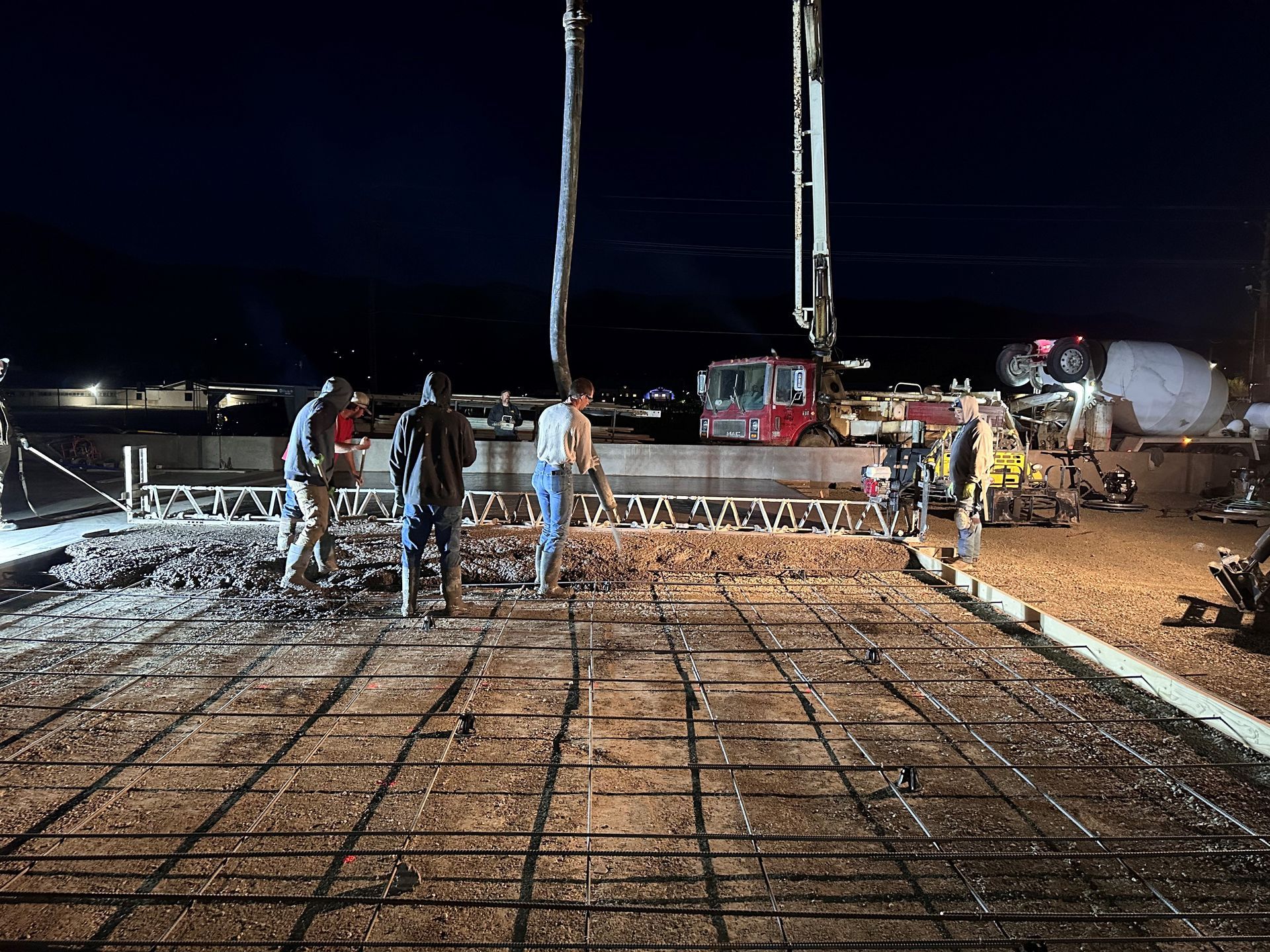 A group of construction workers are working on a concrete floor at night.