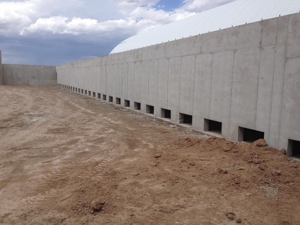 A large concrete wall with holes in it is in the middle of a dirt field.