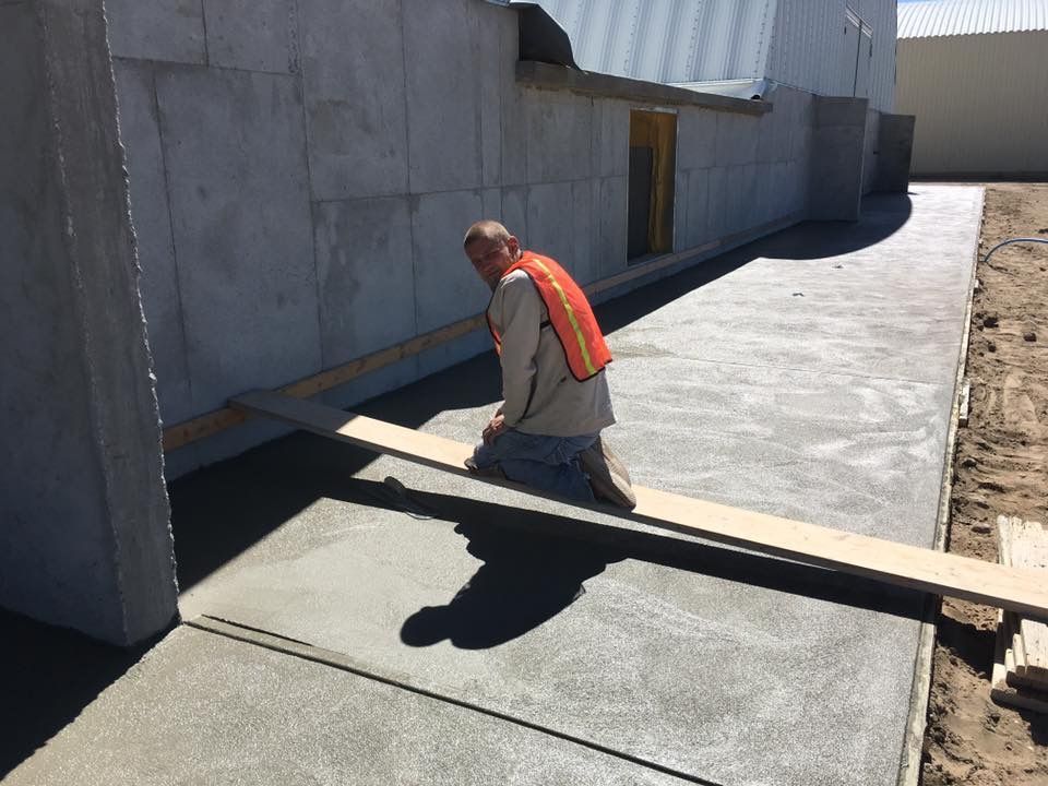 A construction worker is spreading concrete on the ground with a trowel.