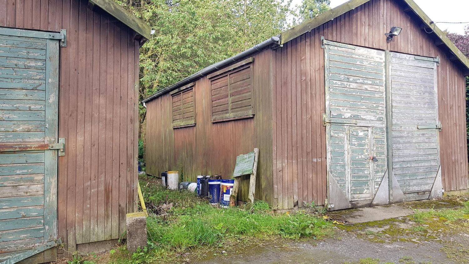 Two wooden sheds with green doors are sitting next to each other in a grassy area.