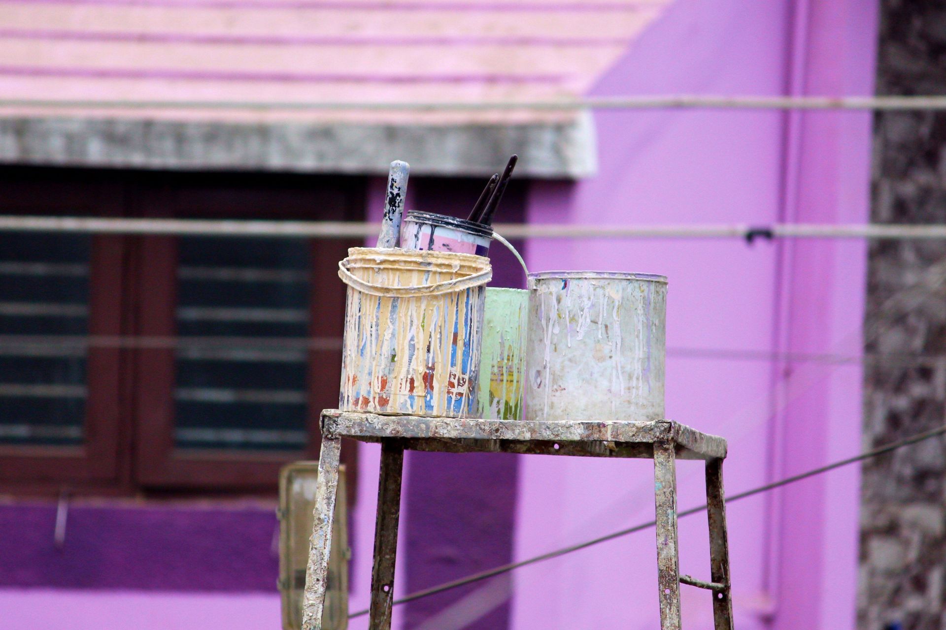 Two buckets of paint are sitting on a wooden stool in front of a purple building.
