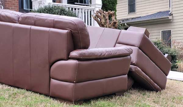 A brown leather couch is laying on the grass in front of a house.