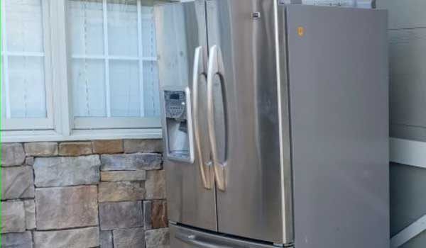 A stainless steel refrigerator is sitting in front of a stone wall.