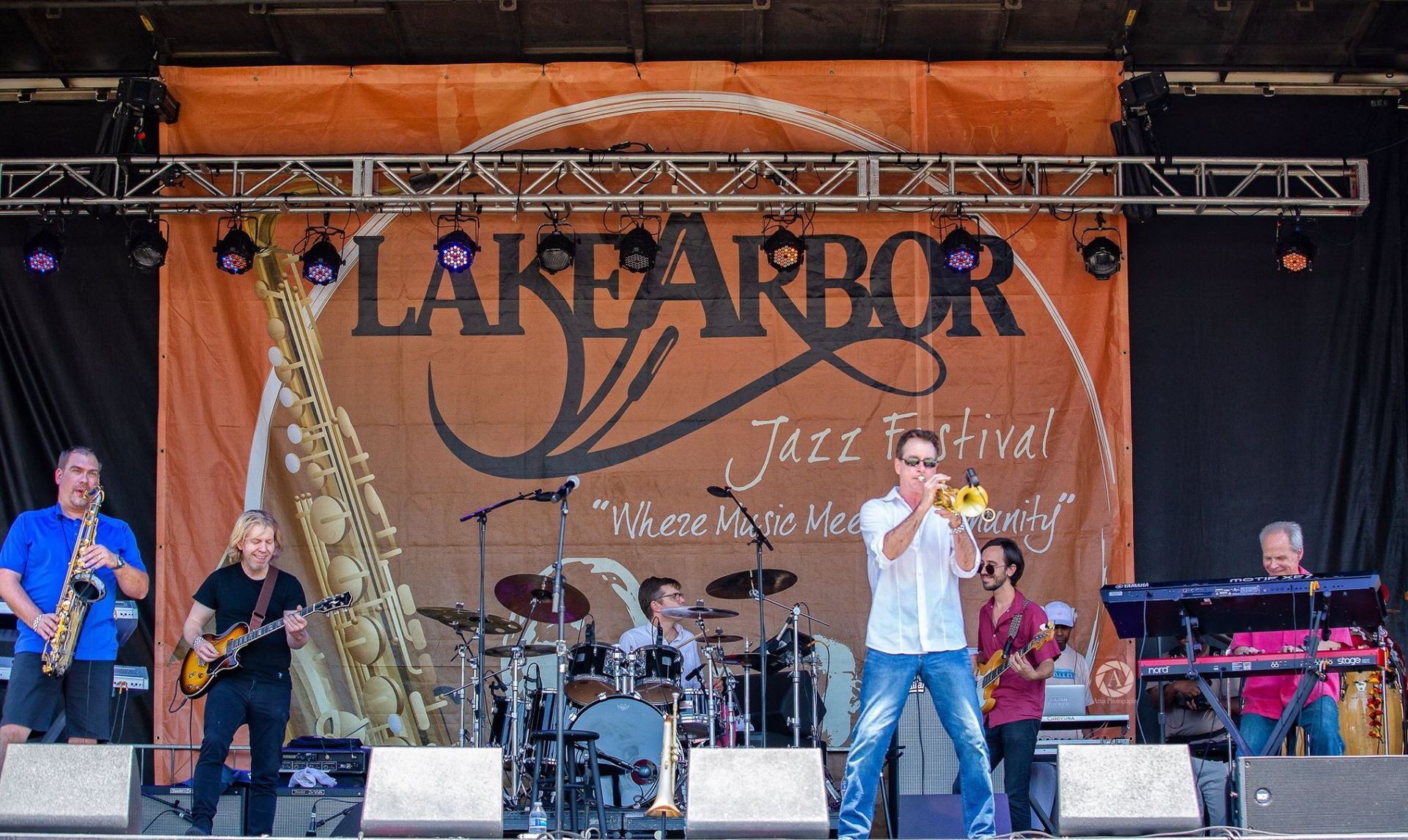 Trumpeter Rob Zinn and group of people are standing on a stage in front of a large sign that says lake arbor jazz festival