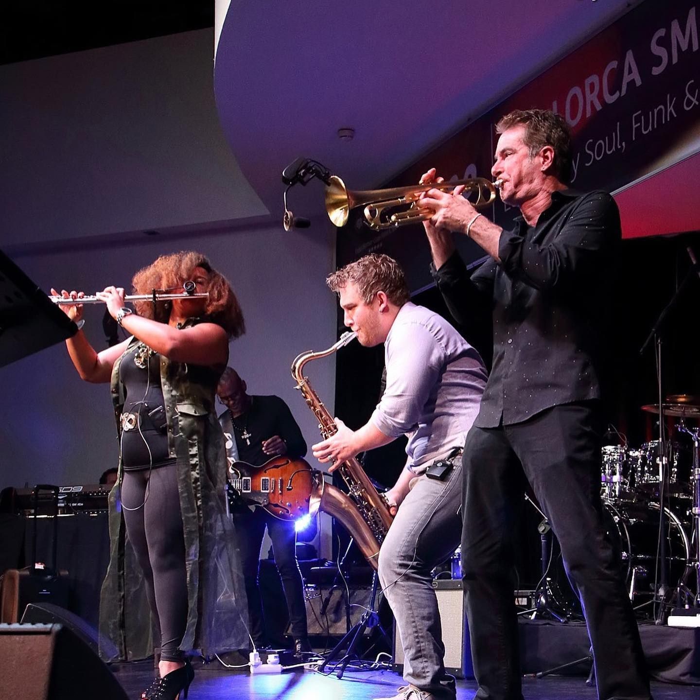 Rob Zinn playing a trumpet and a Ragan Whiteside playing a flute in front of a sign that says maorca jazz fest