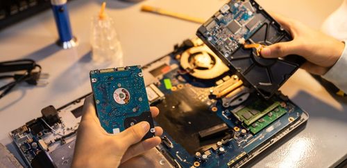 Hands removing a hard drive from a laptop, showing its internal components on a table.