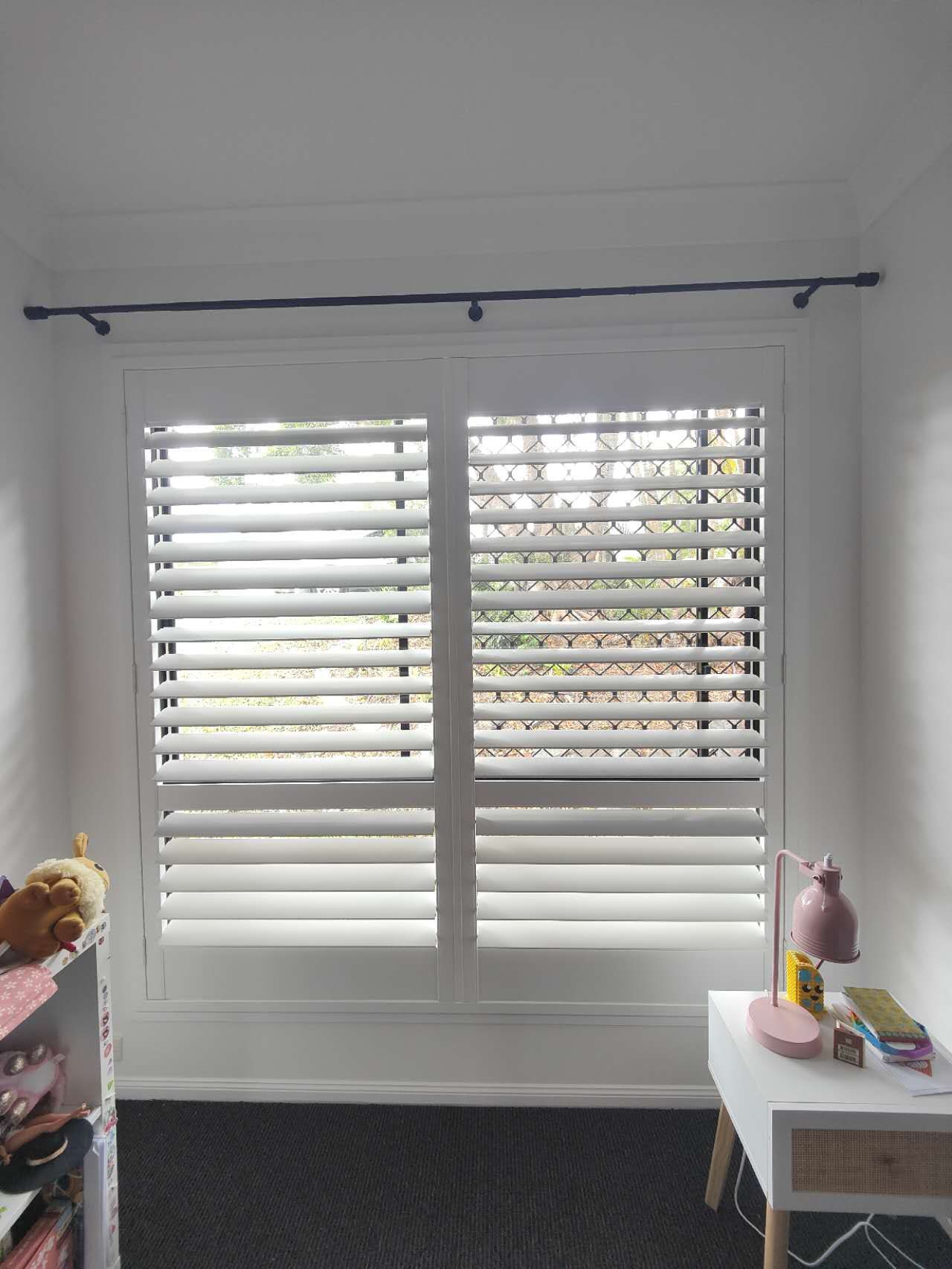 A room with white shutters on the windows and a desk.