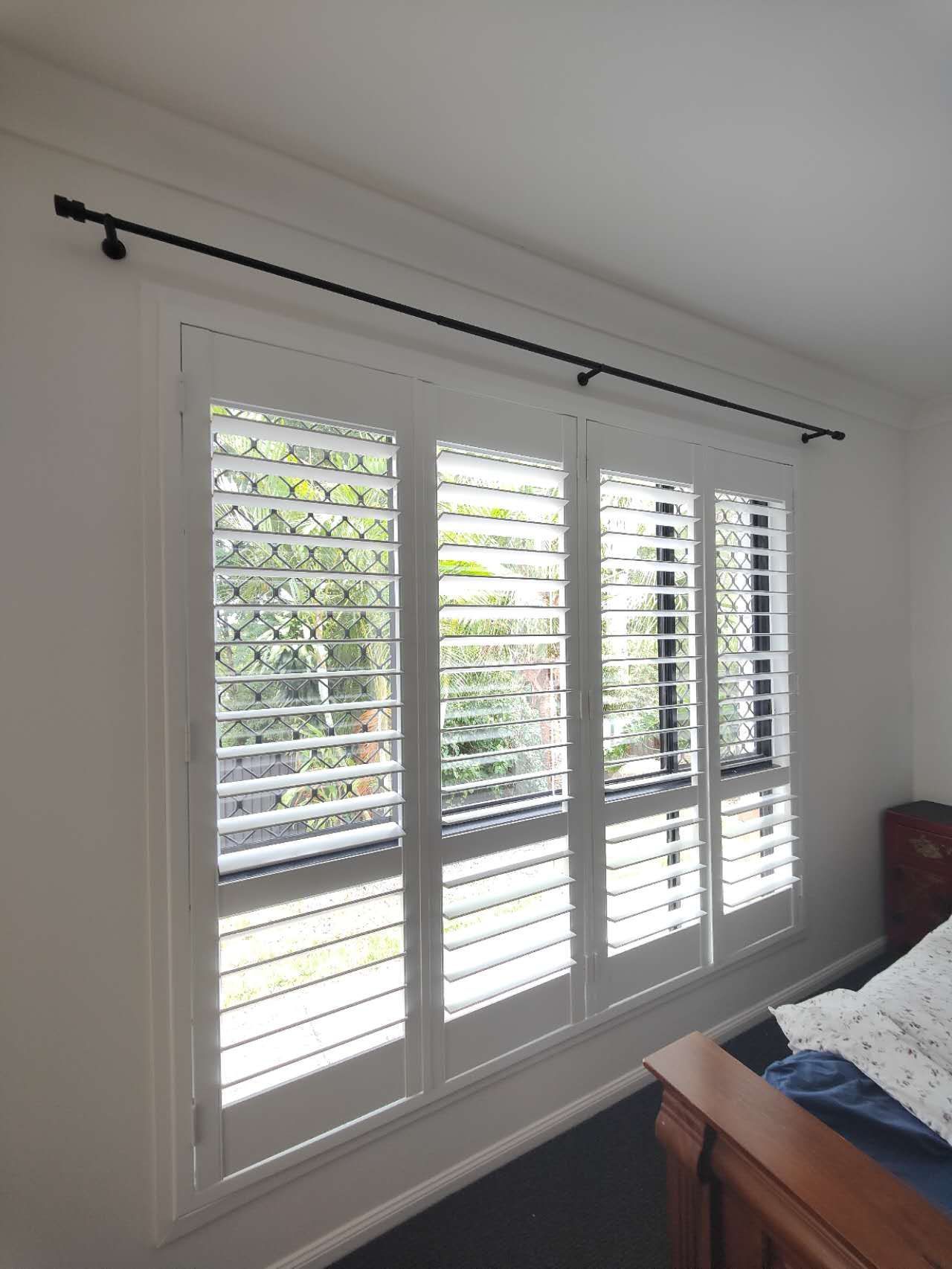 A bedroom with white shutters on the windows and a bed.