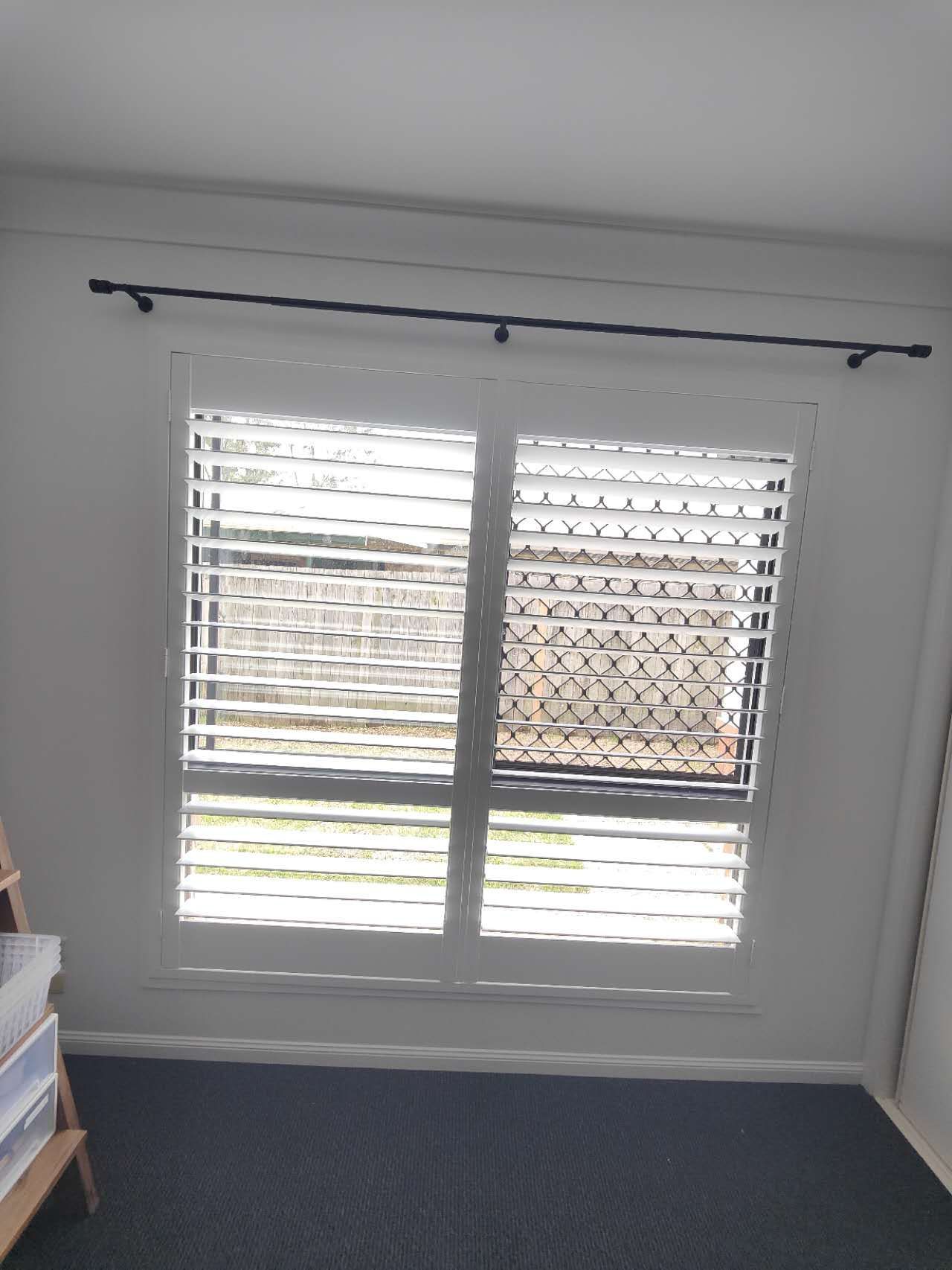 A bedroom with a large window with shutters on it.