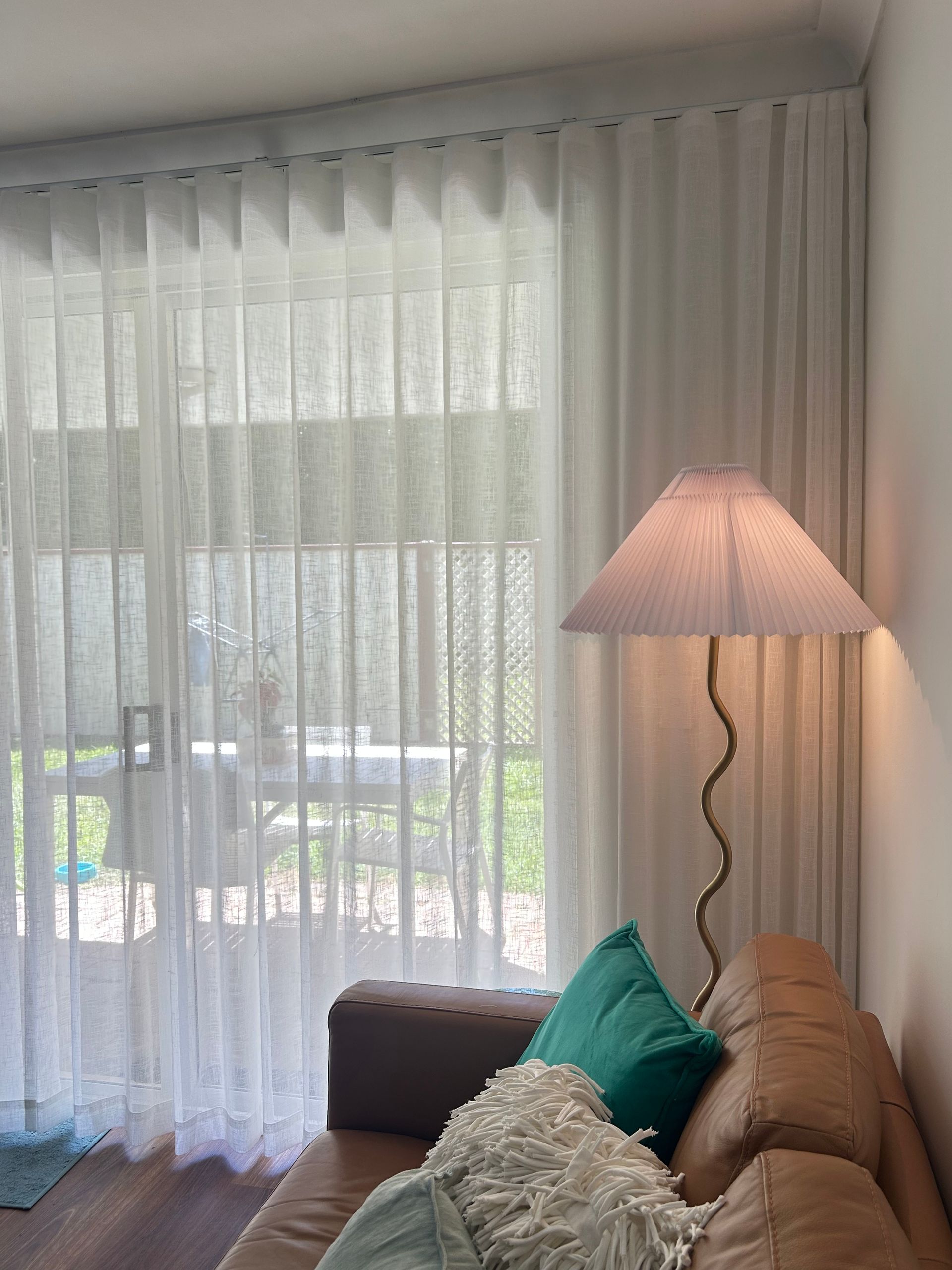 A living room with a couch , lamp and sheer curtains.