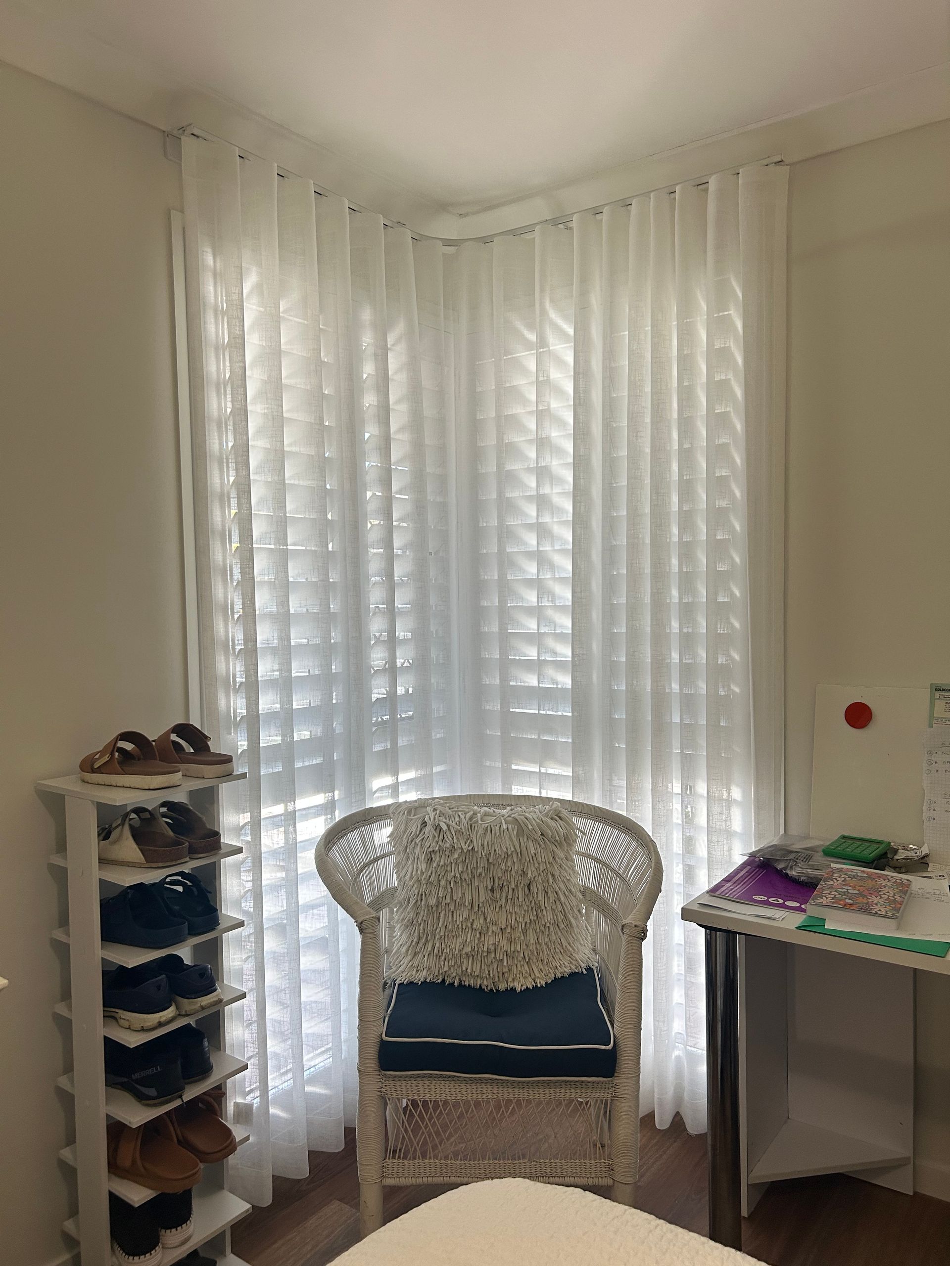 A chair is sitting in front of a window in a room with white curtains.