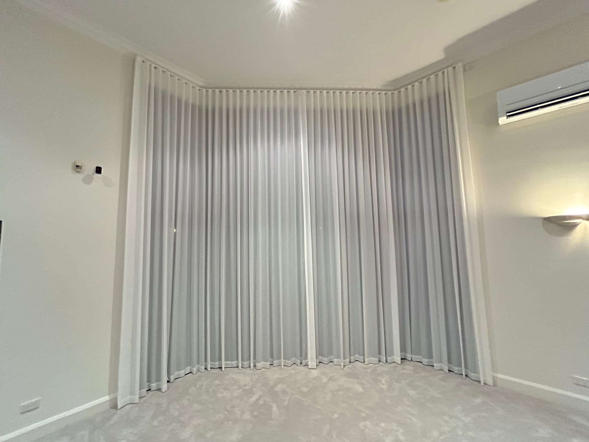 A bedroom with a large window and white curtains.