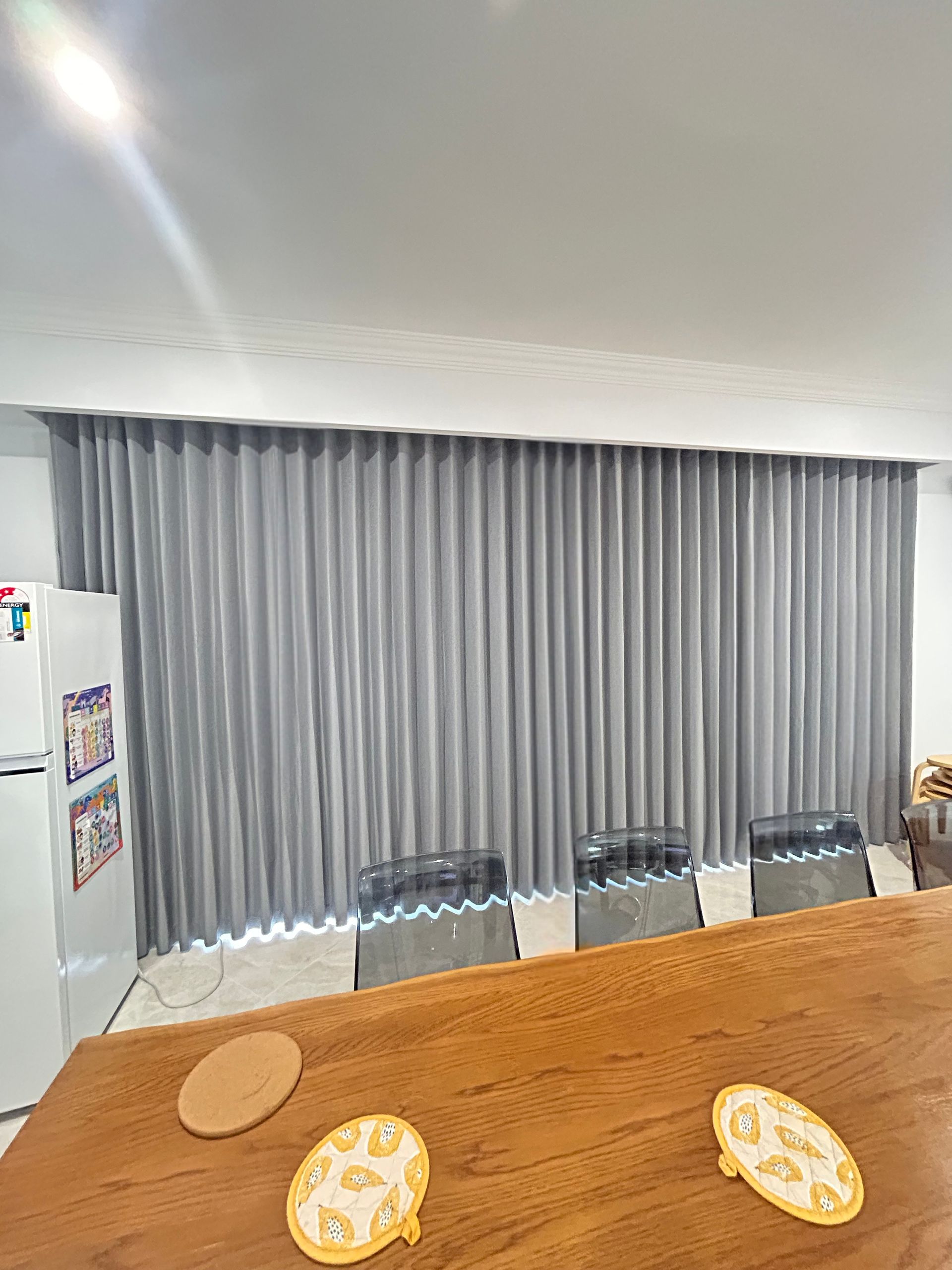 A dining room with a table , chairs , curtains and a refrigerator.