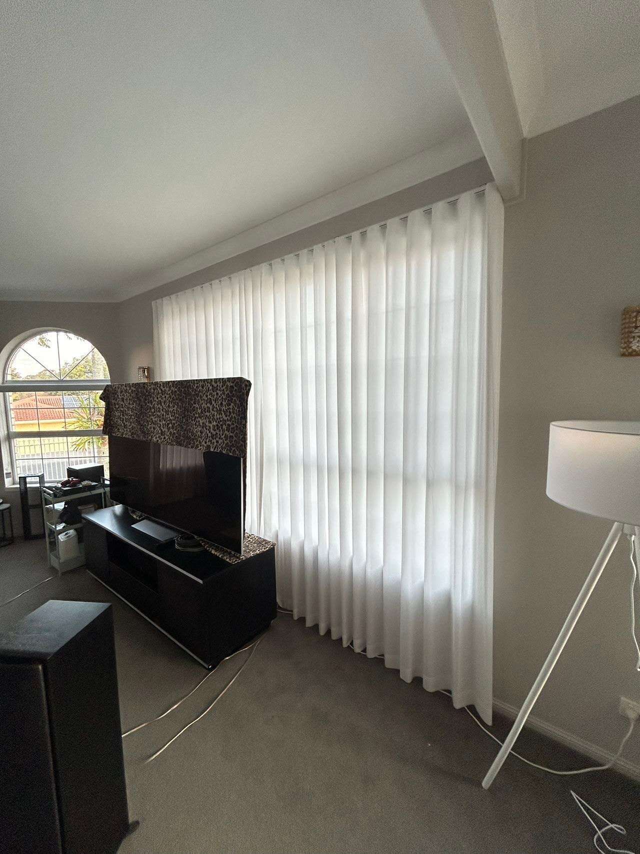 A living room with white curtains and a flat screen tv