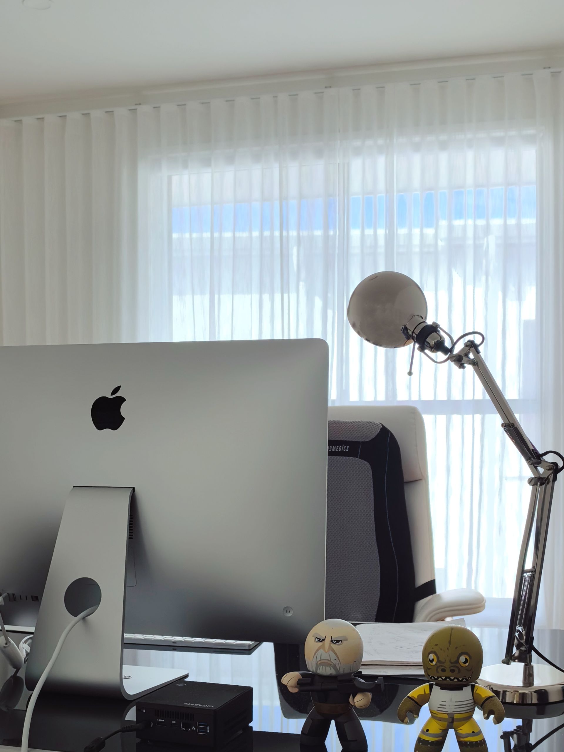 An apple computer is sitting on a desk in front of a window.