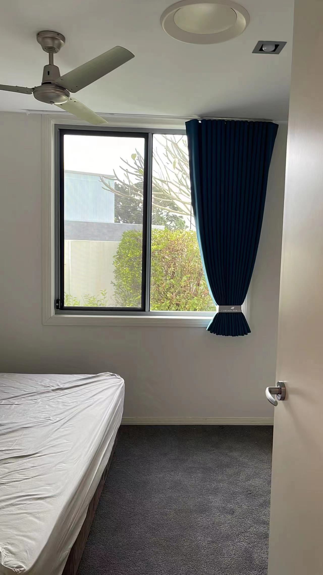 A bedroom with a bed , ceiling fan , window and curtains.