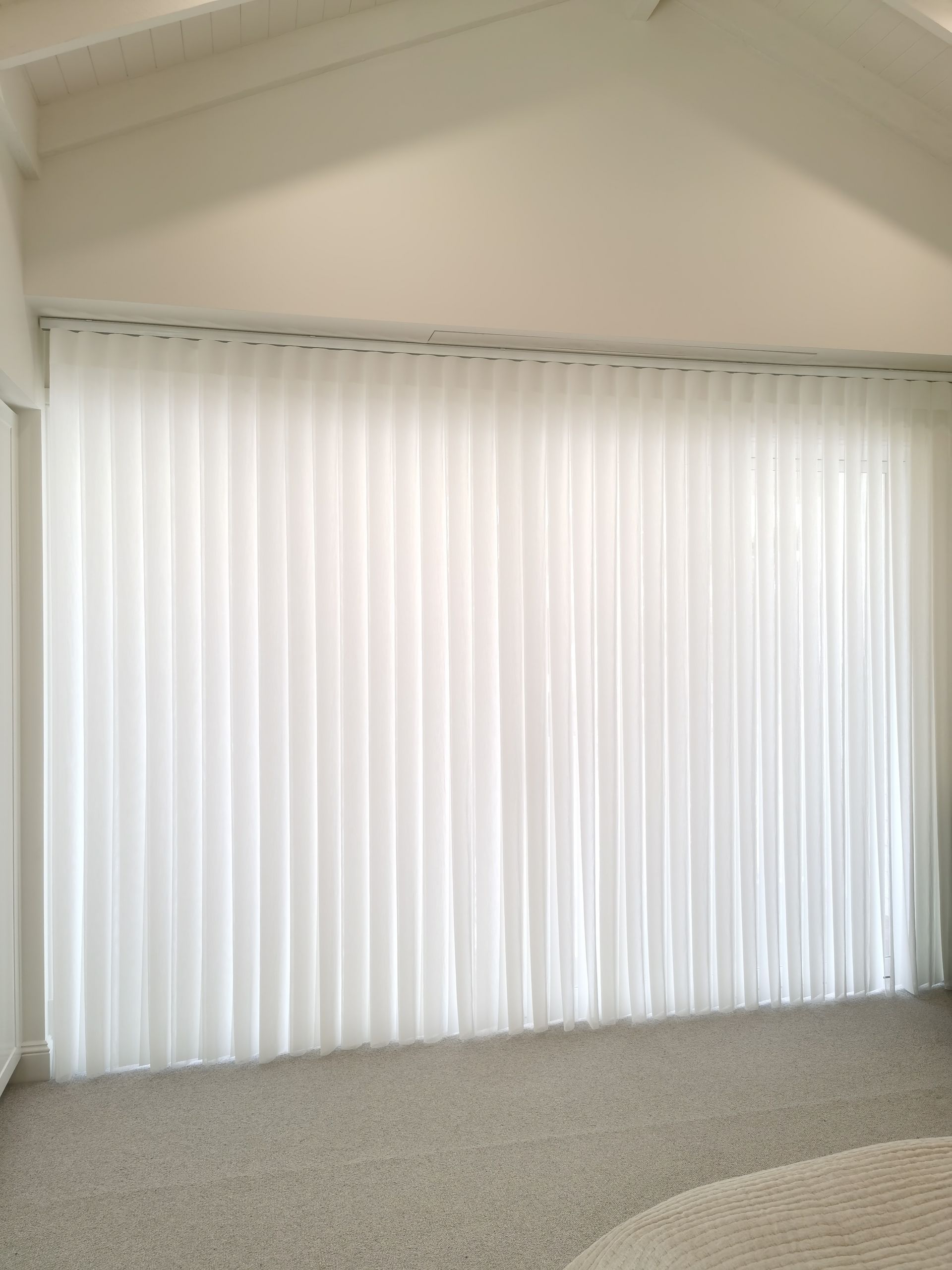 A living room with a large window and white vertical blinds.