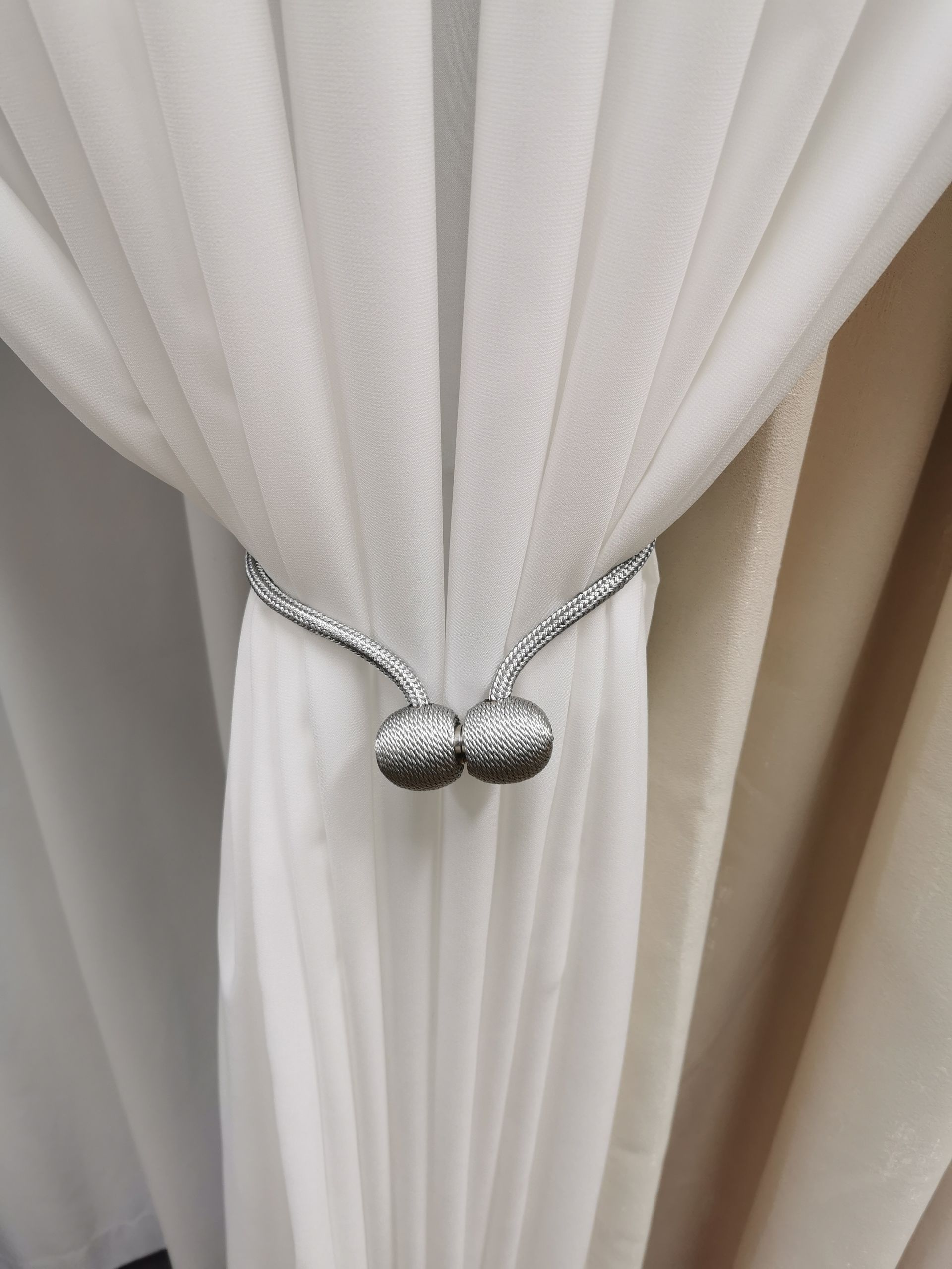 A close up of a white curtain with a silver tie back.
