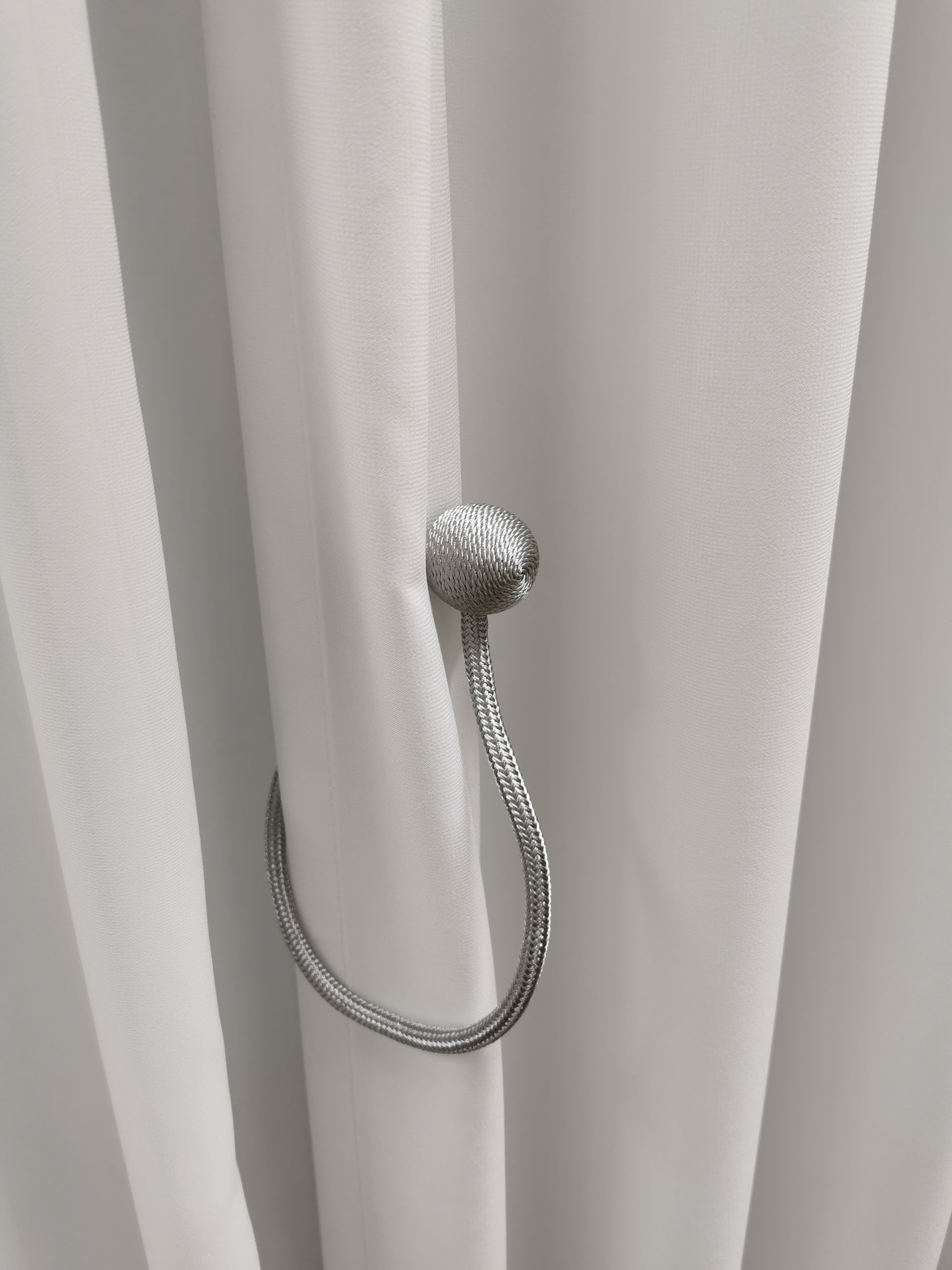 A close up of a silver curtain tie back on a white curtain.