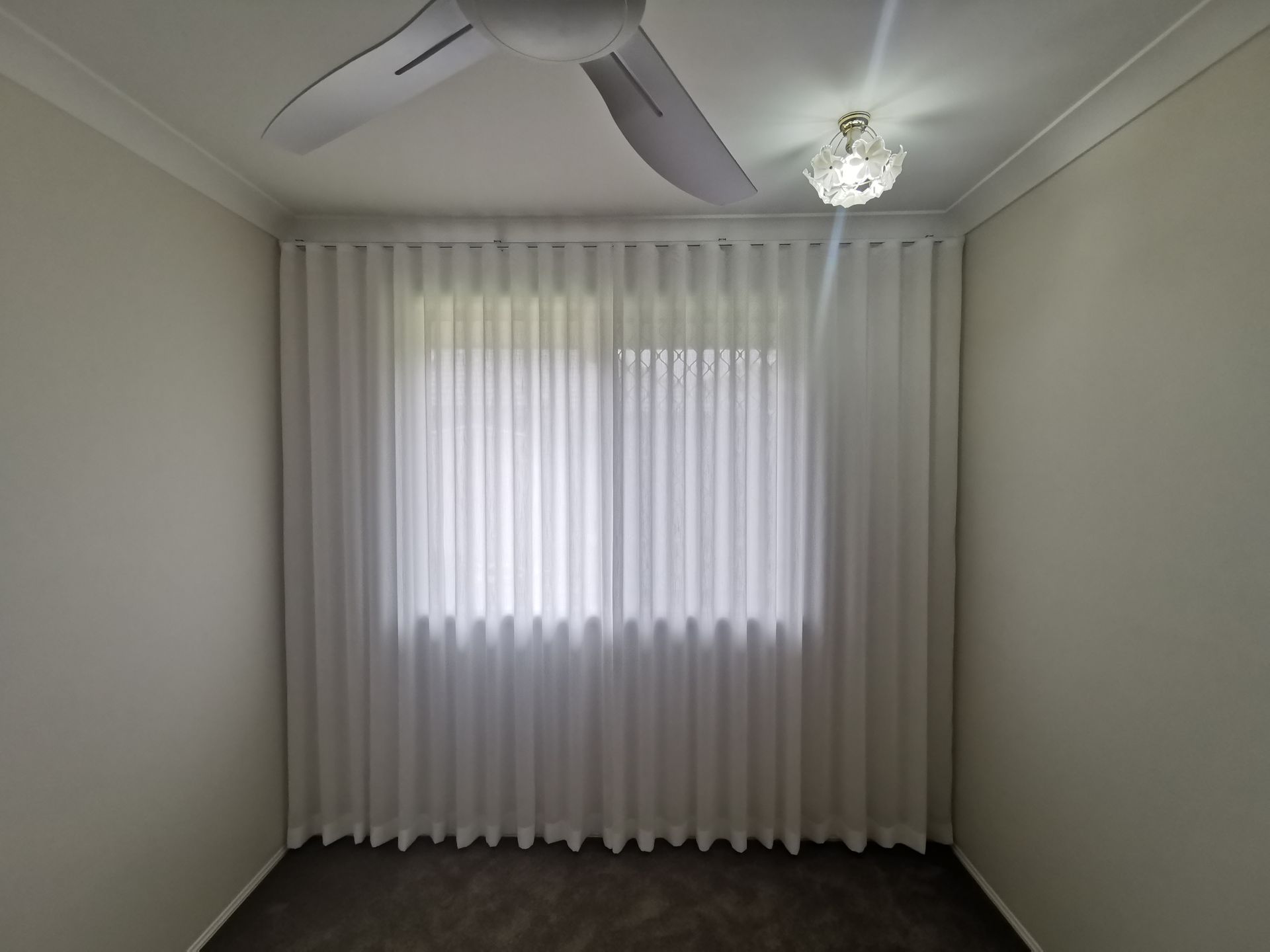 A bedroom with white curtains and a ceiling fan