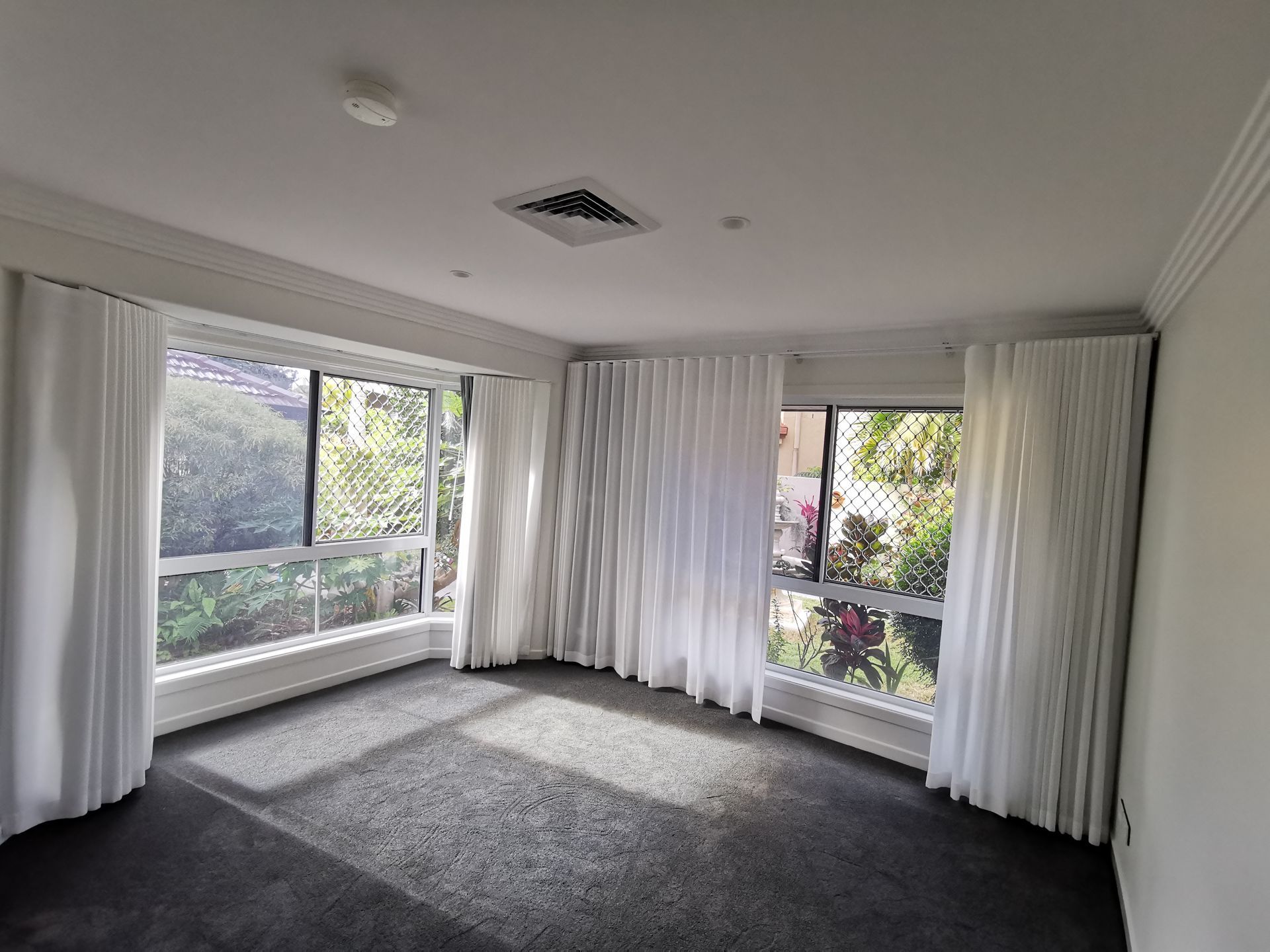 An empty room with a lot of windows and white curtains.