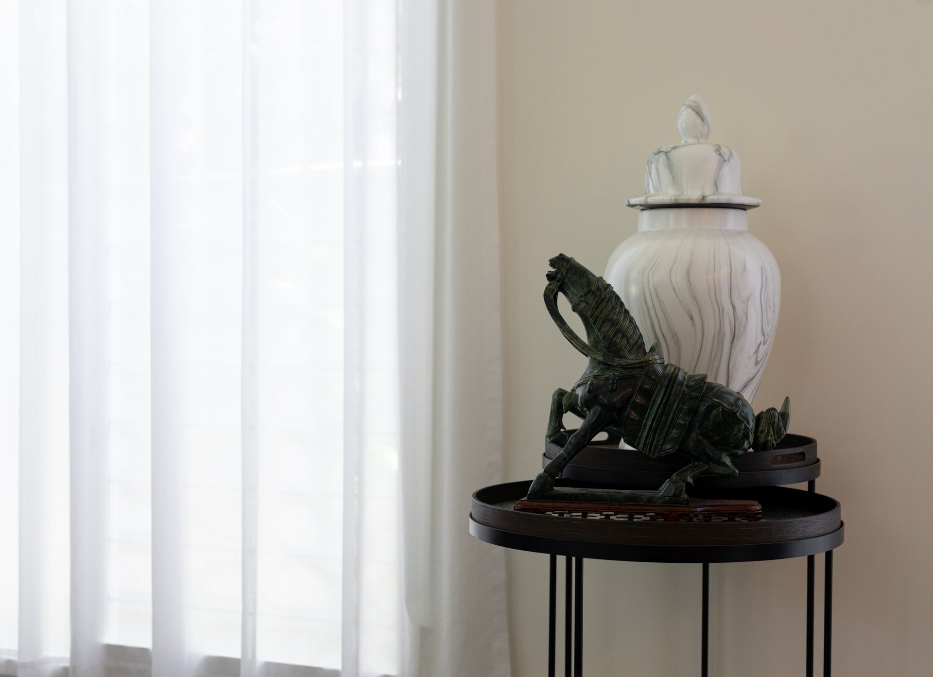 A table with a vase and a statue on it in front of a window.