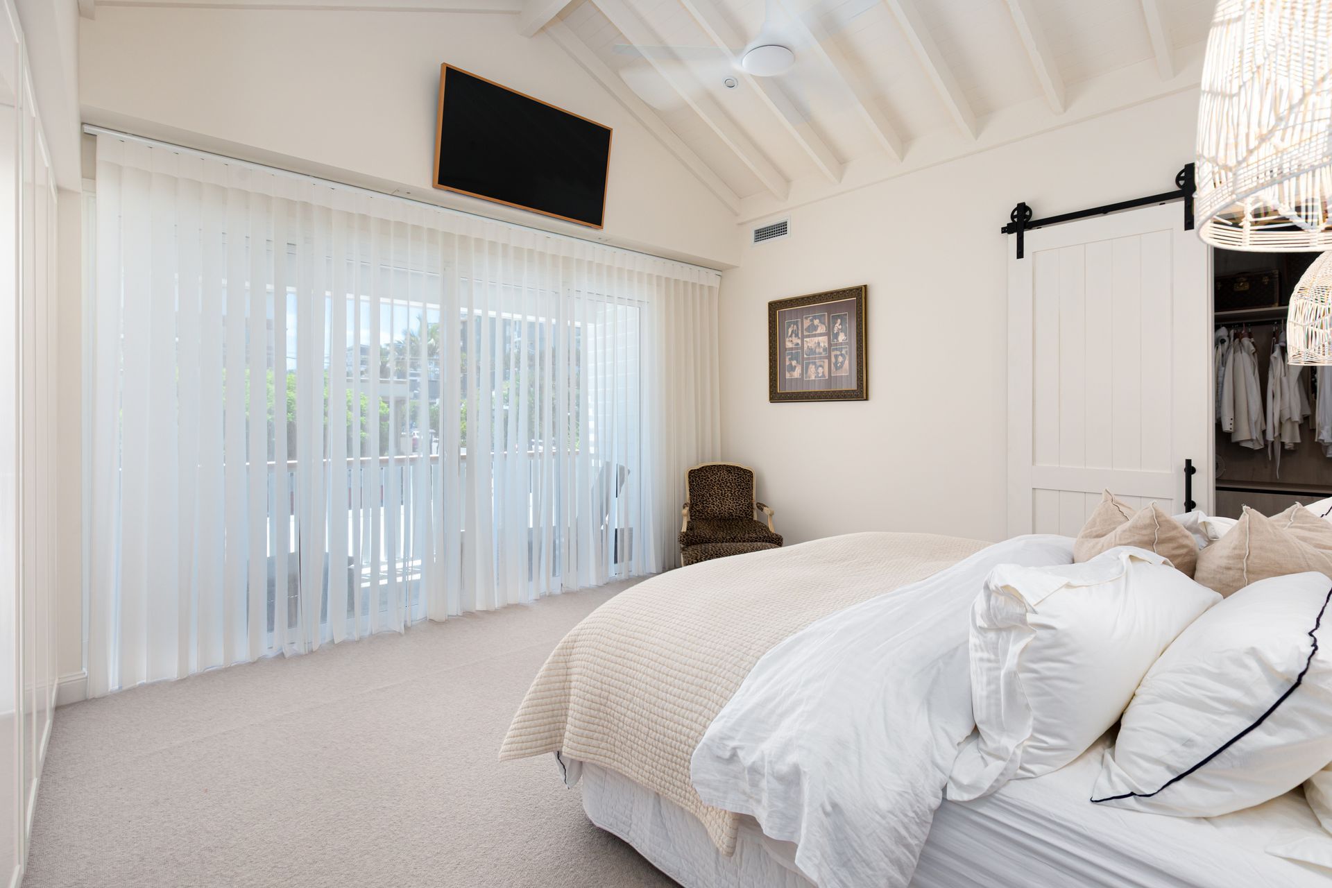 A bedroom with a bed , chair , television and sliding glass doors.