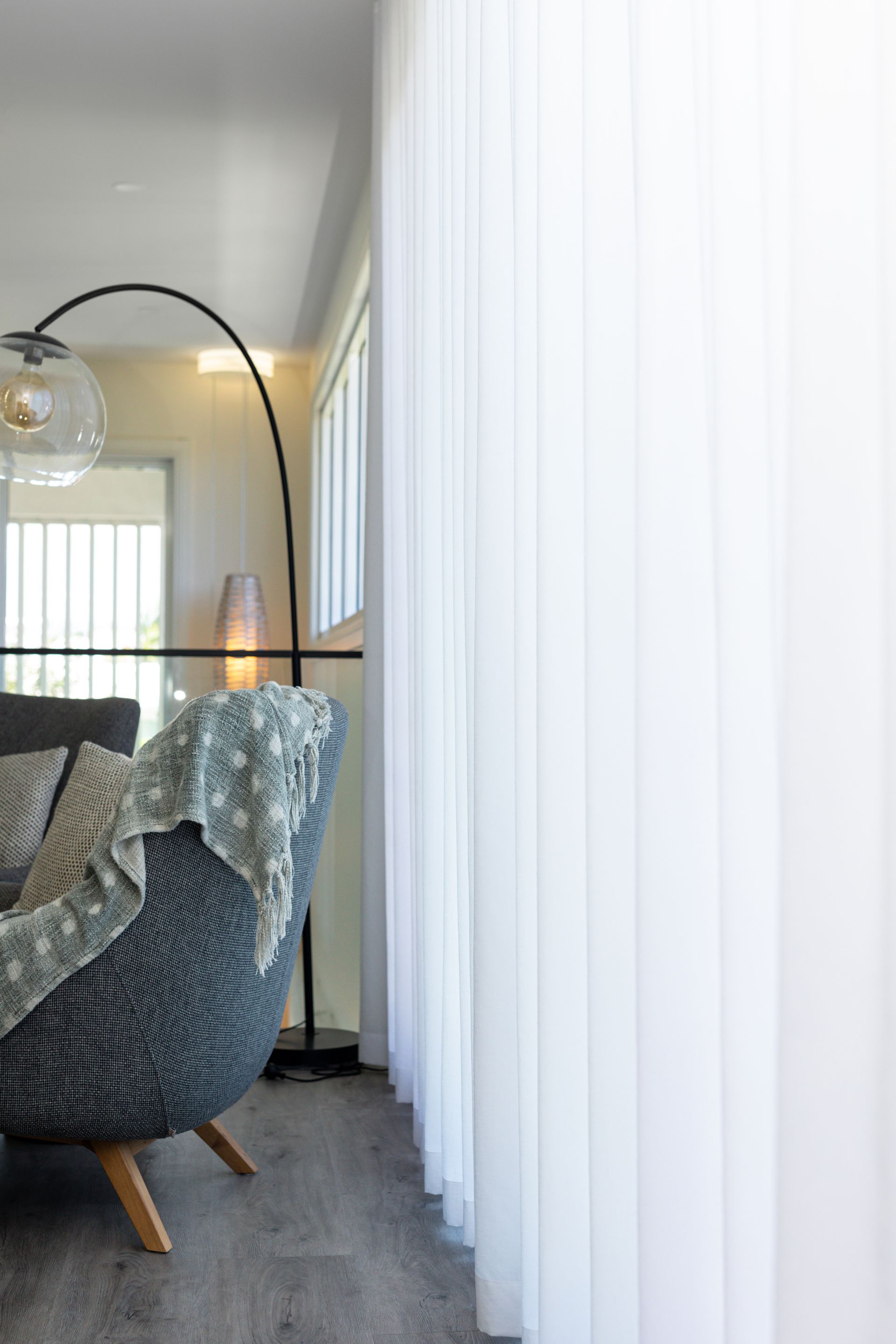 A living room with a couch , chair , lamp and white curtains.