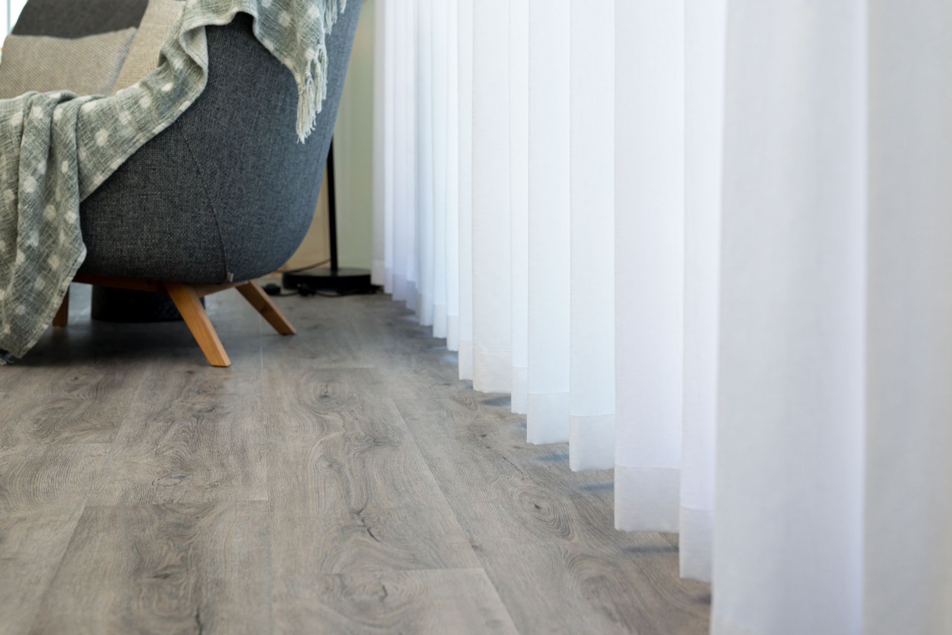 A chair with a blanket on it is sitting next to a window in a living room.