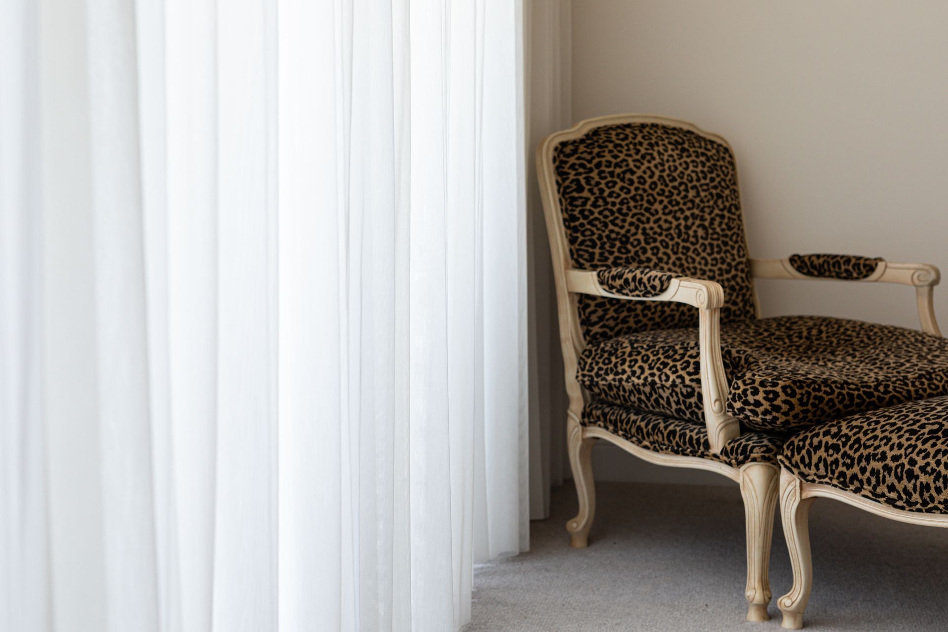 A leopard print chair and ottoman are in a room next to a window.