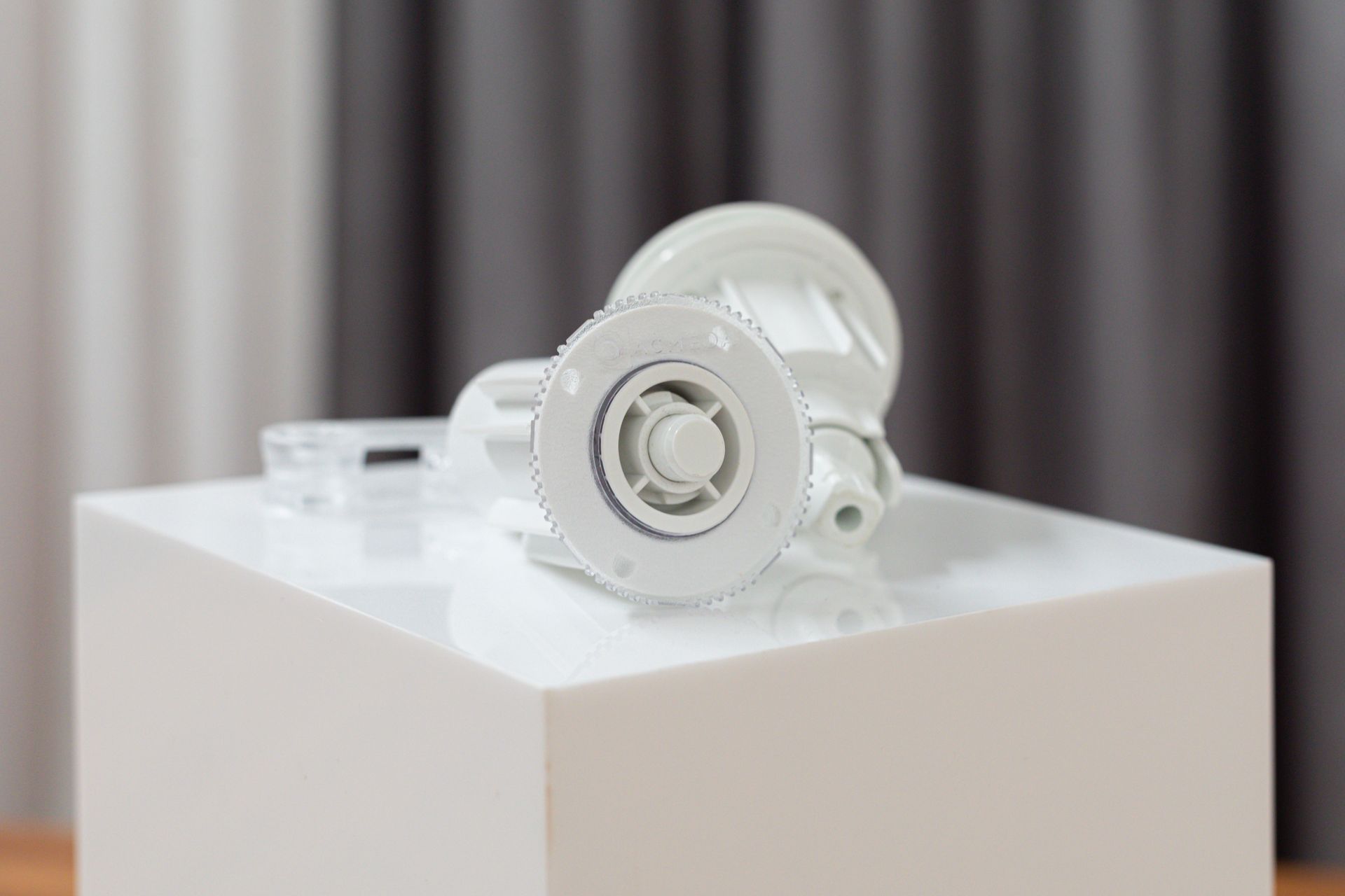 A white object is sitting on top of a white cube on a table.