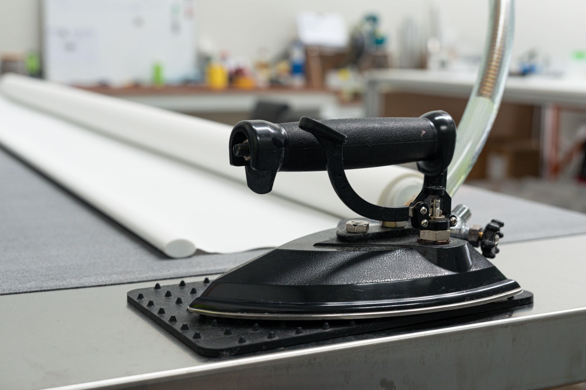 A black iron is sitting on a table next to a roll of fabric.