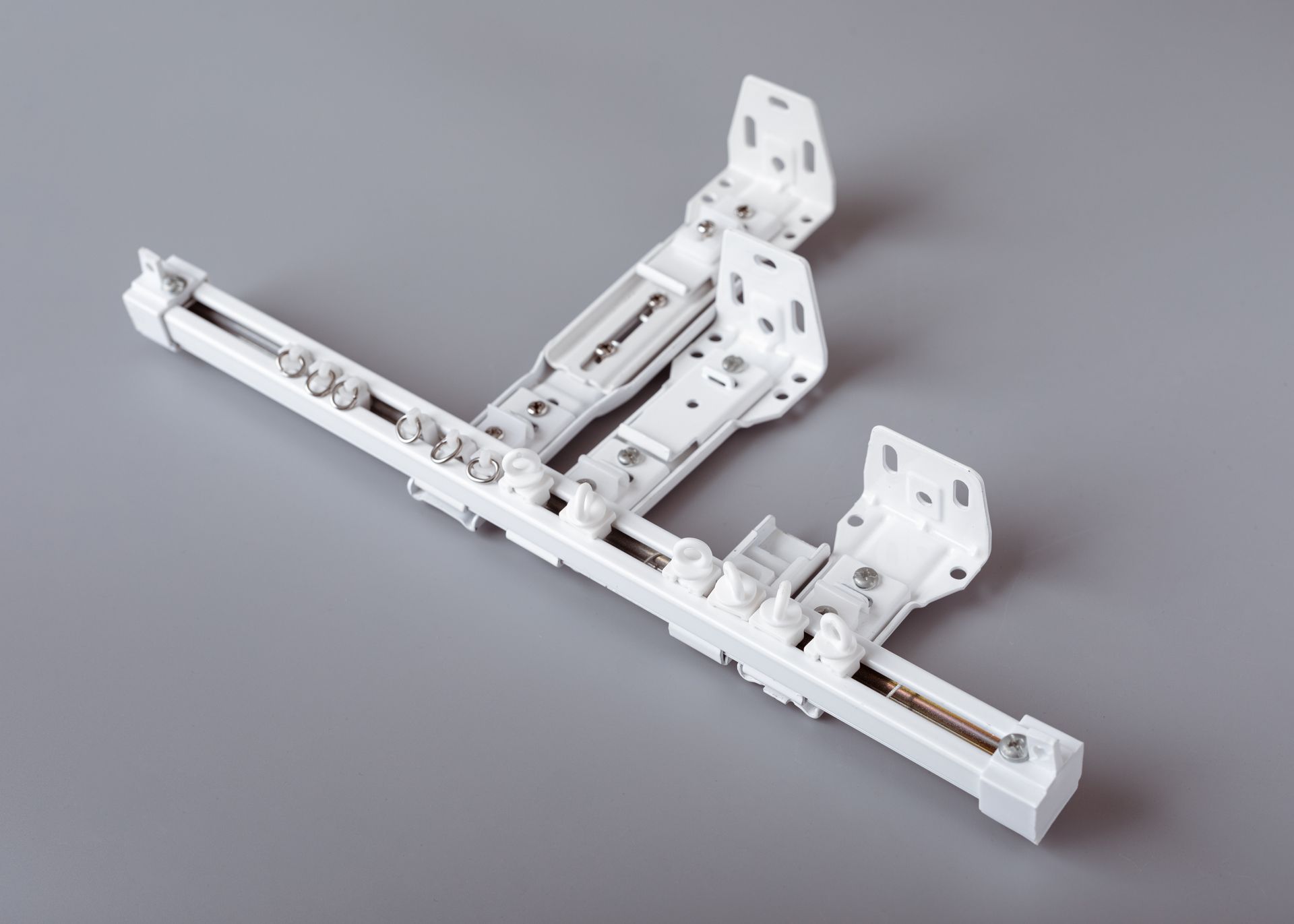A white curtain track is sitting on a gray surface.