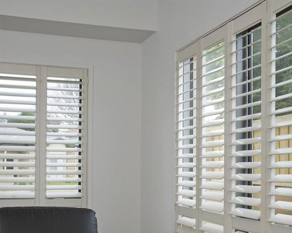 A room with white shutters on the windows and a chair.