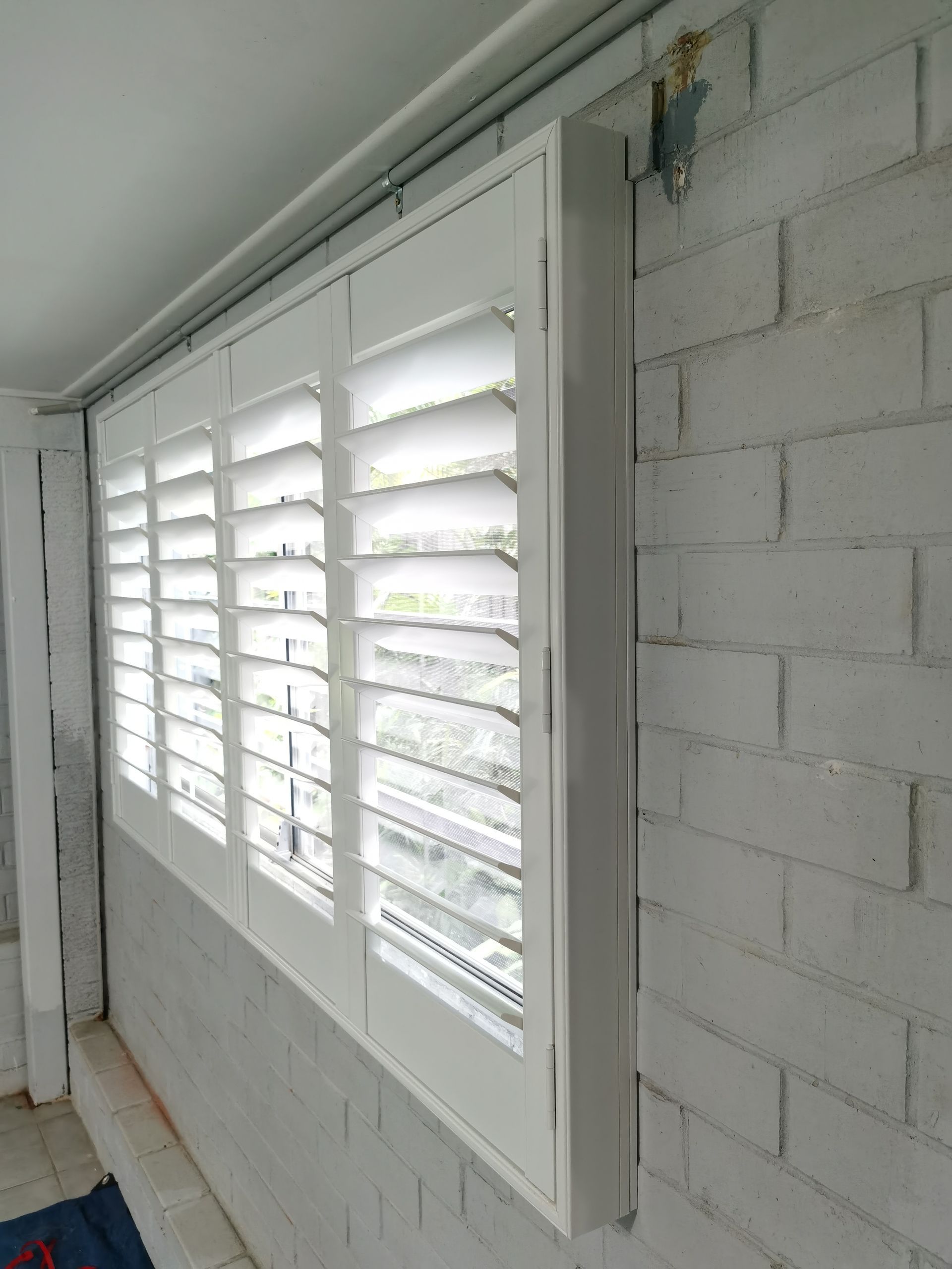 A window with white shutters on a white brick wall.