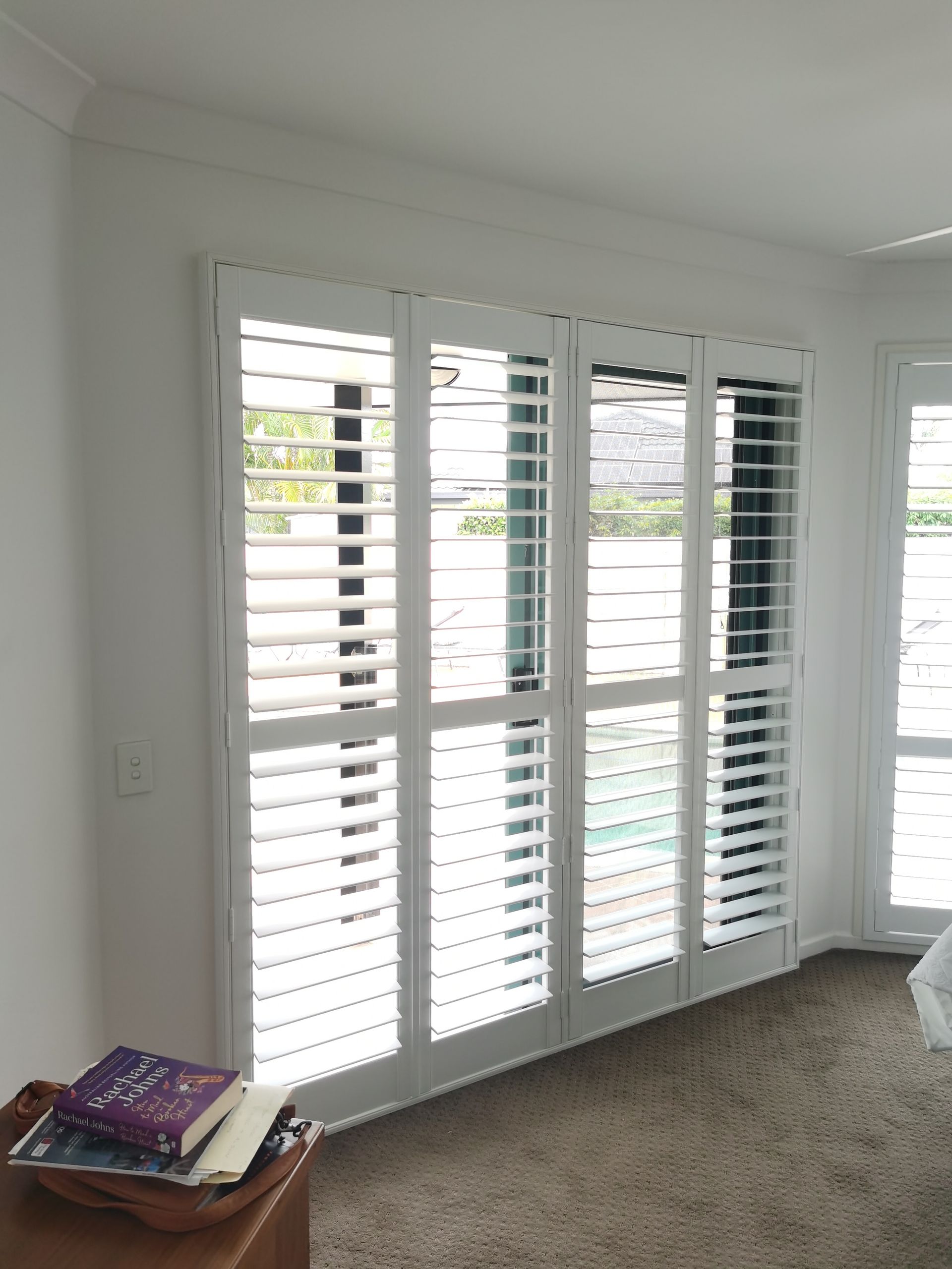 A living room with white shutters on the windows and a table with books on it.