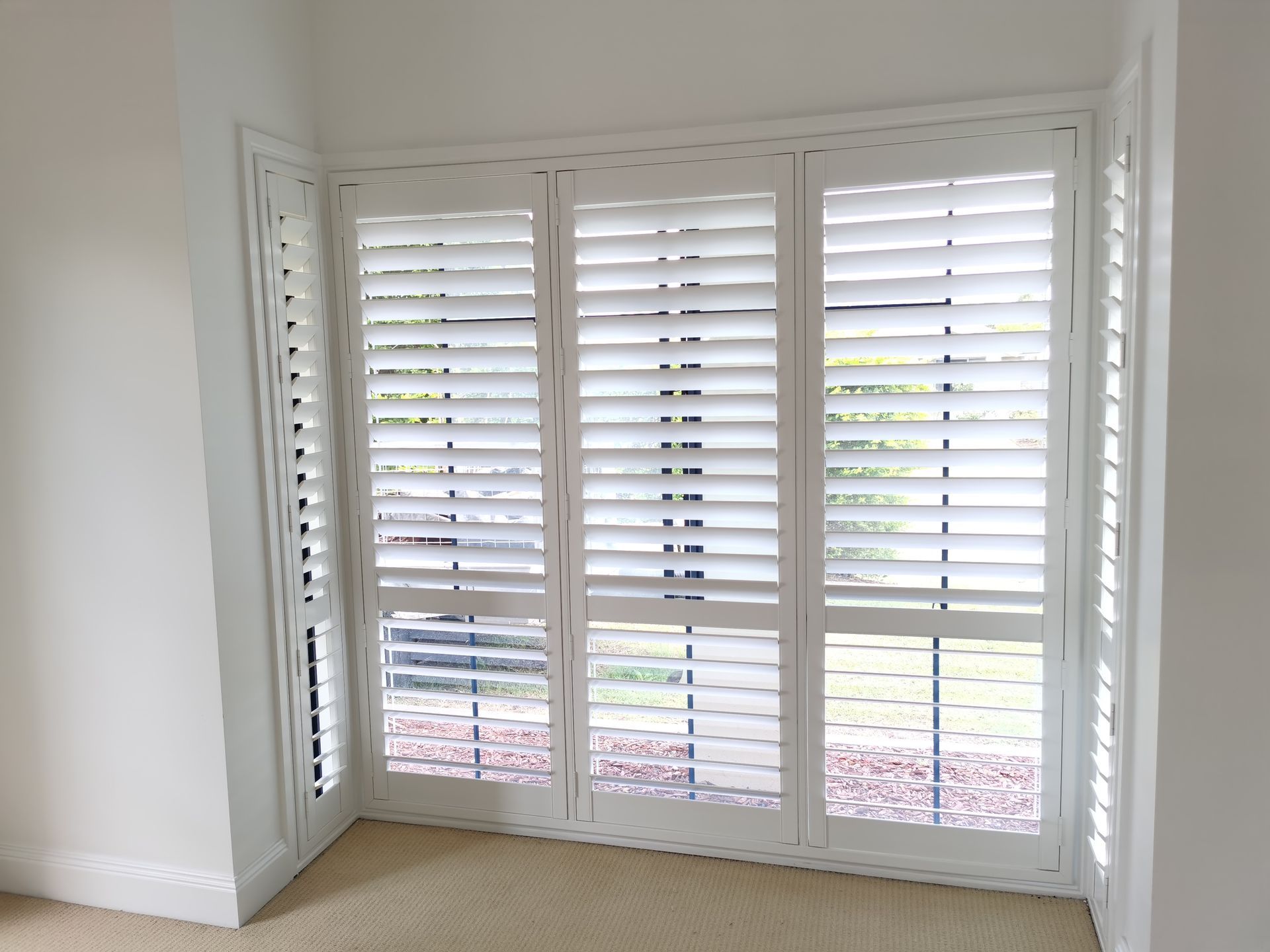 An empty room with white shutters on the windows