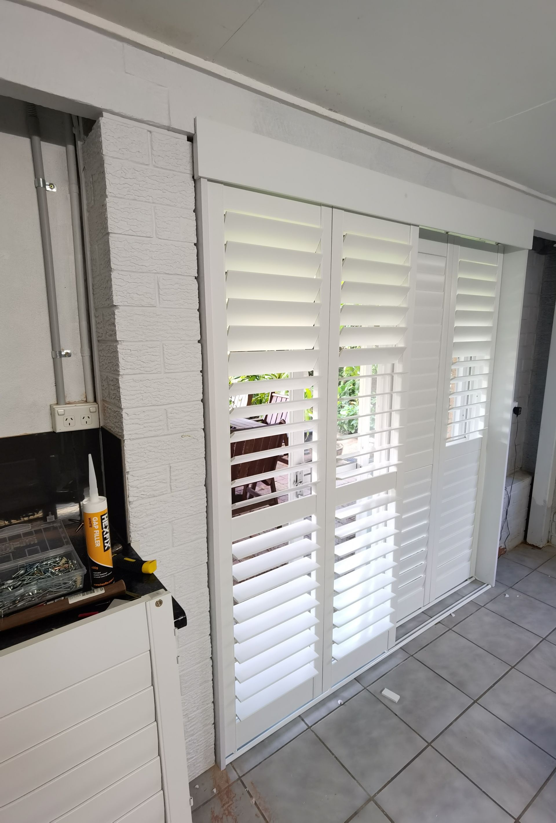A room with a sliding glass door with white shutters on it.