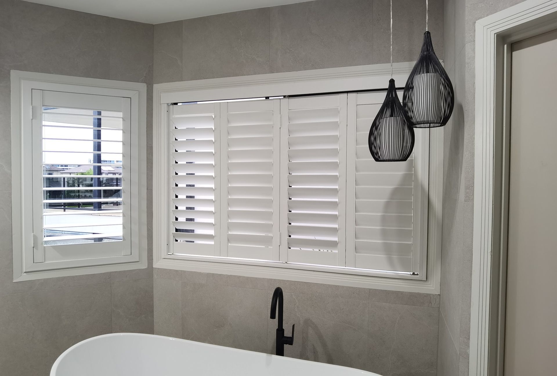 There is a bathtub in the bathroom with shutters on the windows.