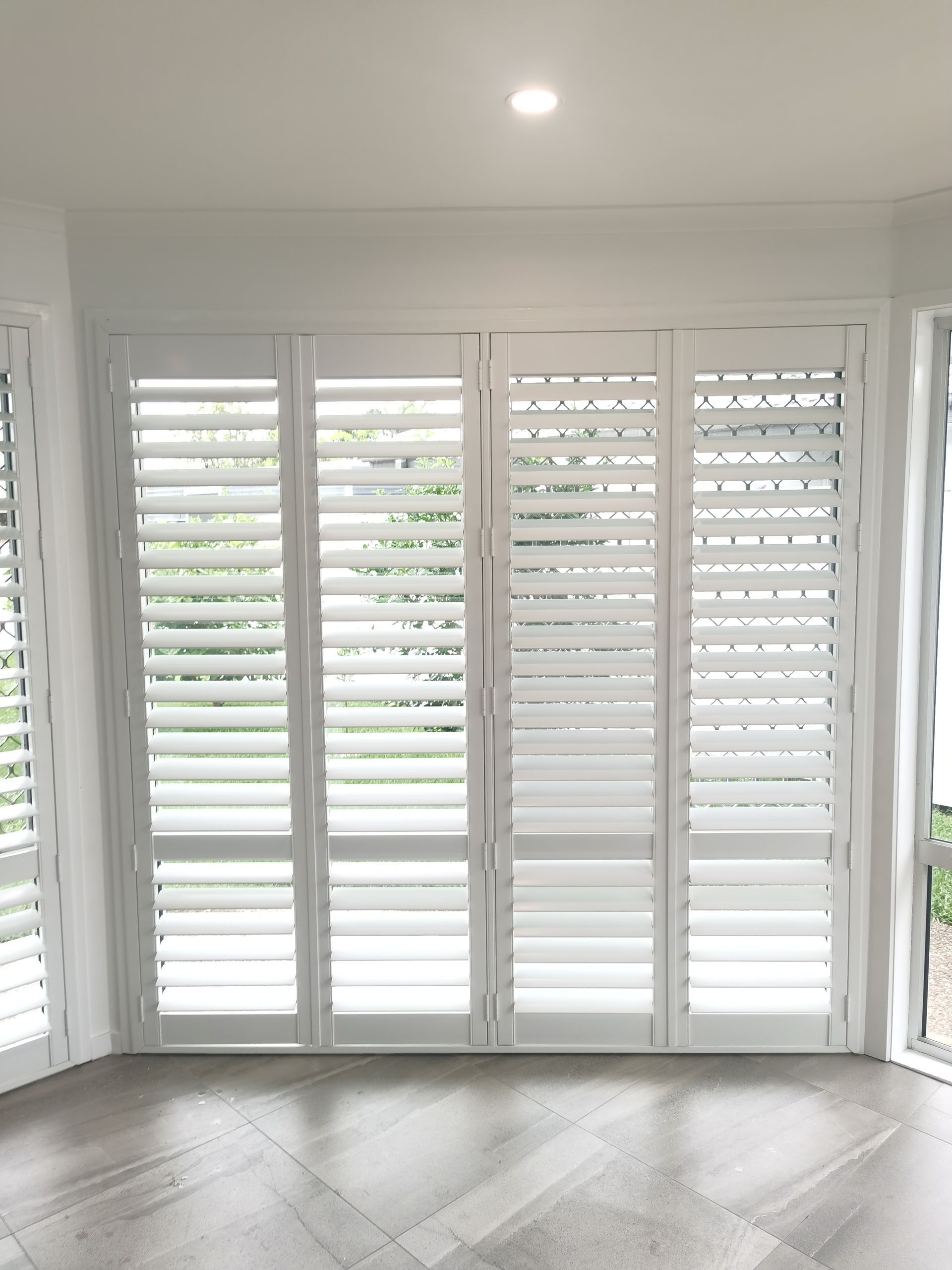 A room with white shutters on the windows and a wooden floor.