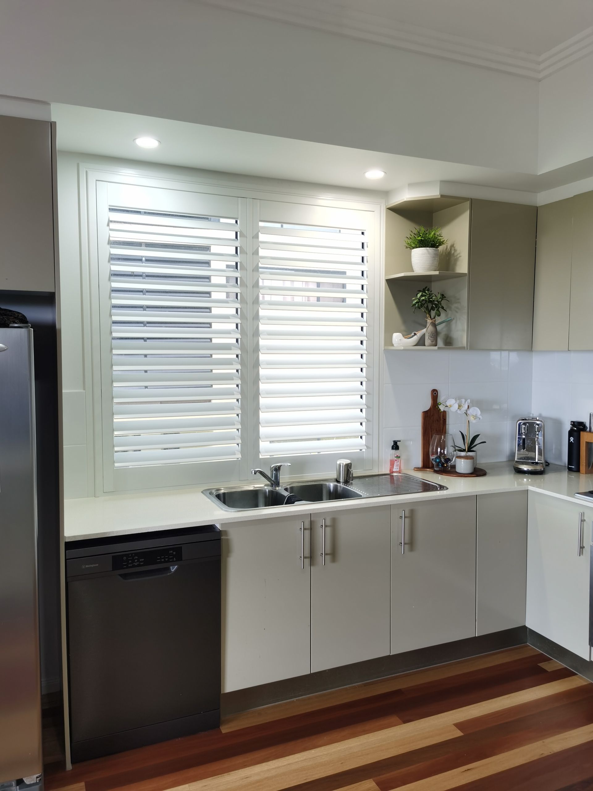 A kitchen with white cabinets , a sink , a refrigerator , a dishwasher and a window.