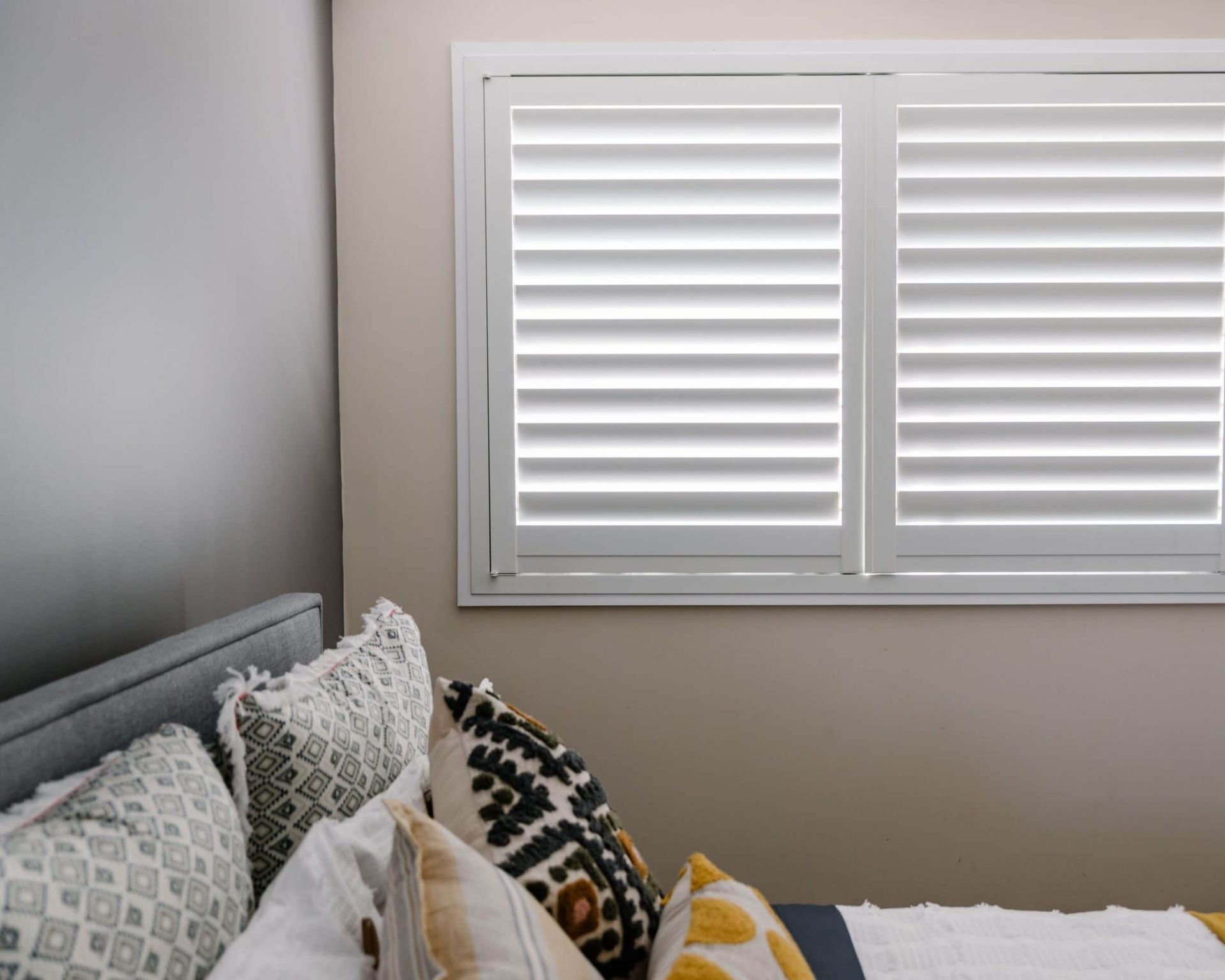 A bedroom with a bed , pillows and a window with shutters.