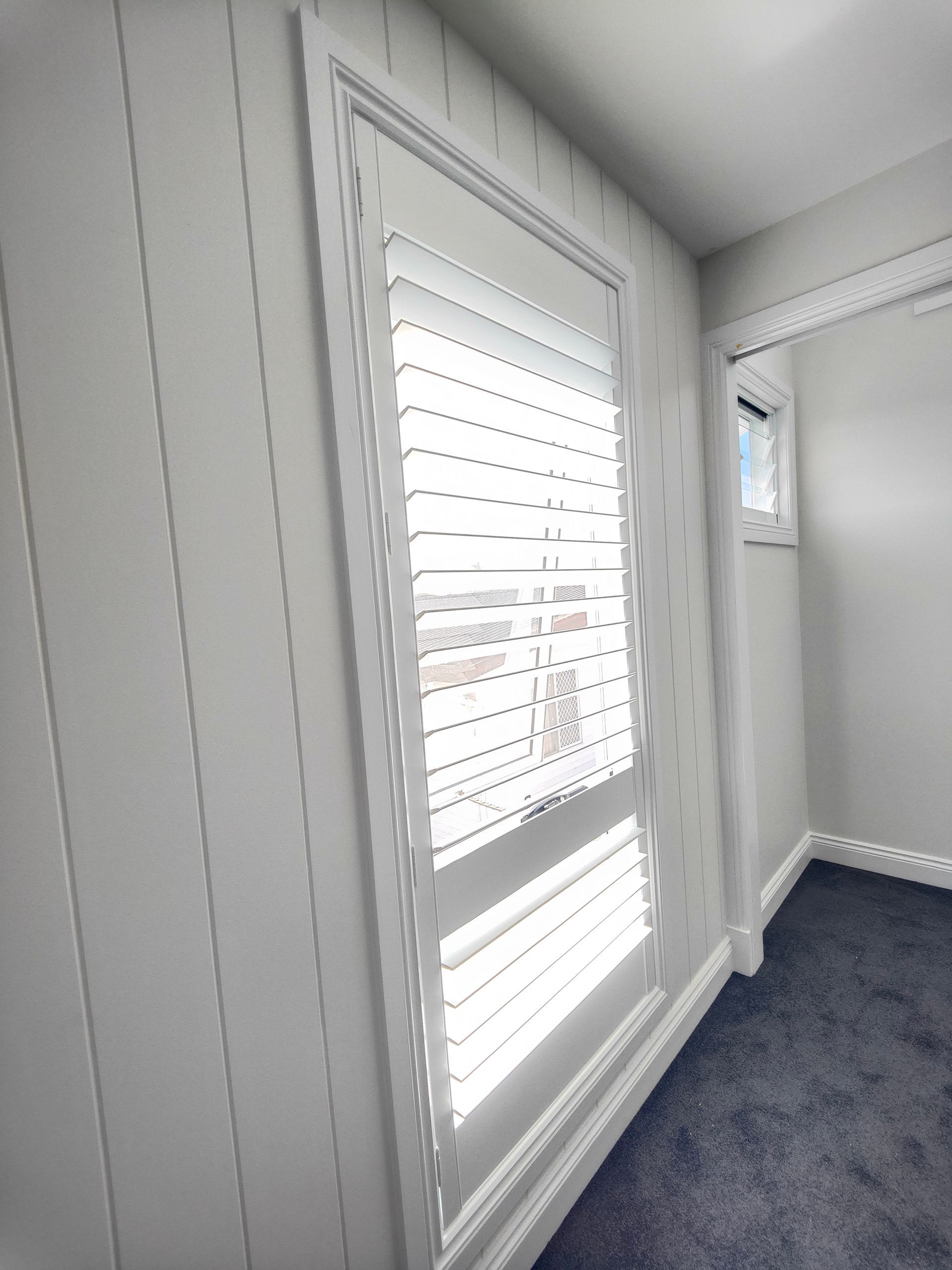 A room with white walls and a window with shutters on it.