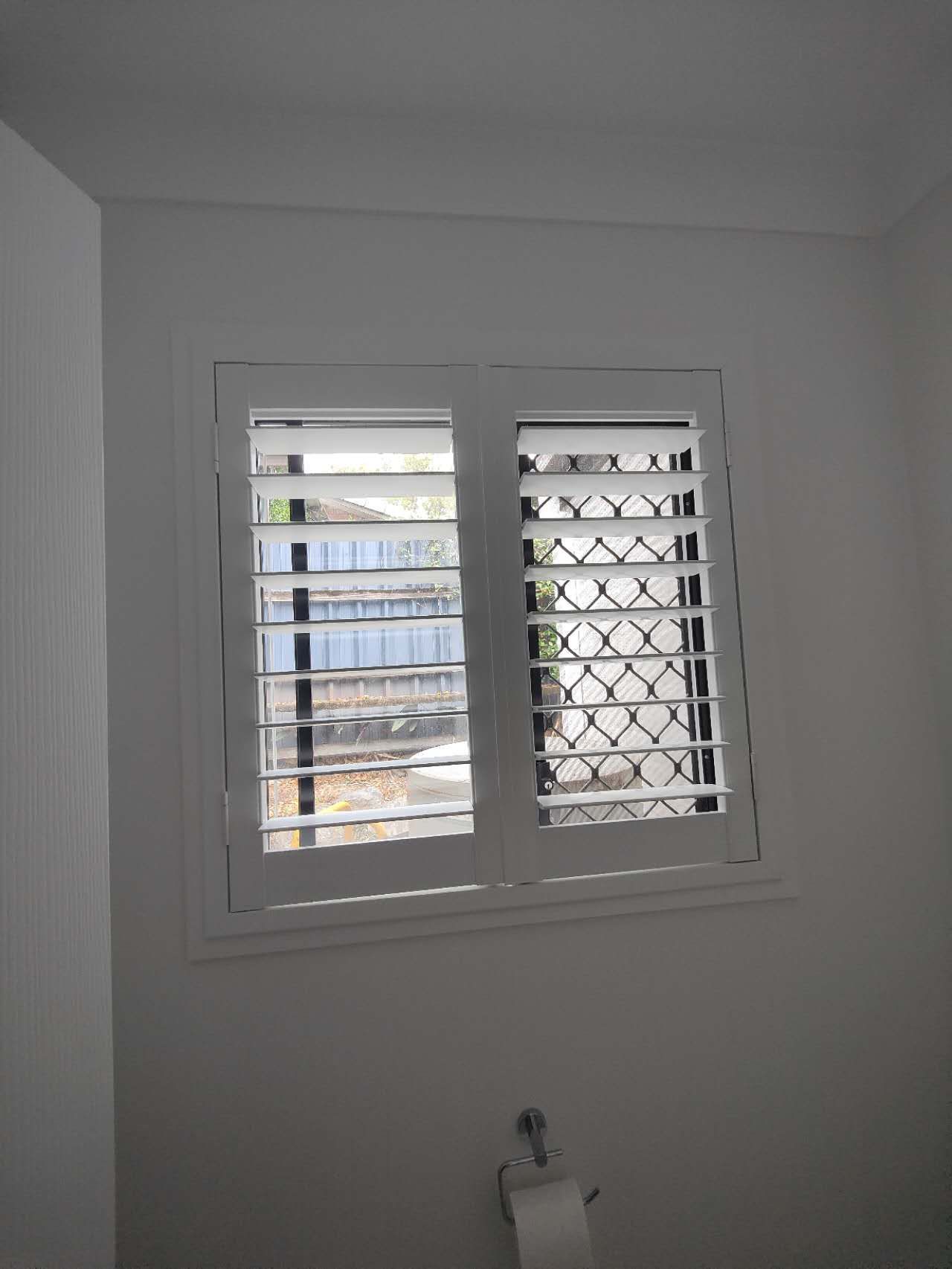 A bathroom window with shutters on it and a toilet paper holder.