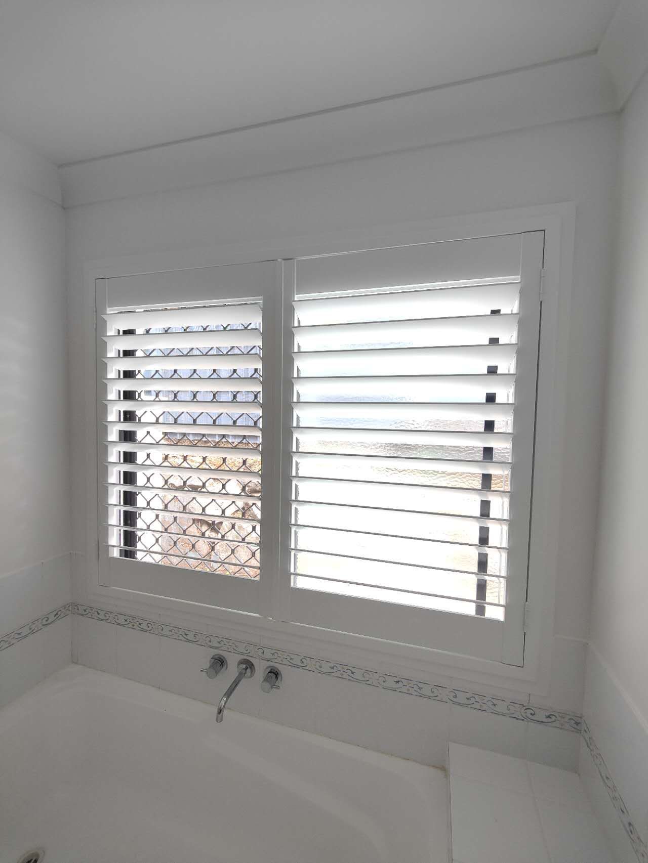A bathroom with a bathtub and a window with shutters on it.
