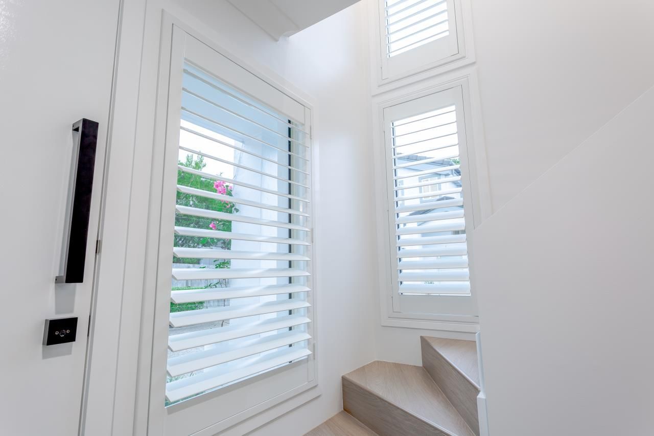 A hallway with stairs and a window with shutters on it.