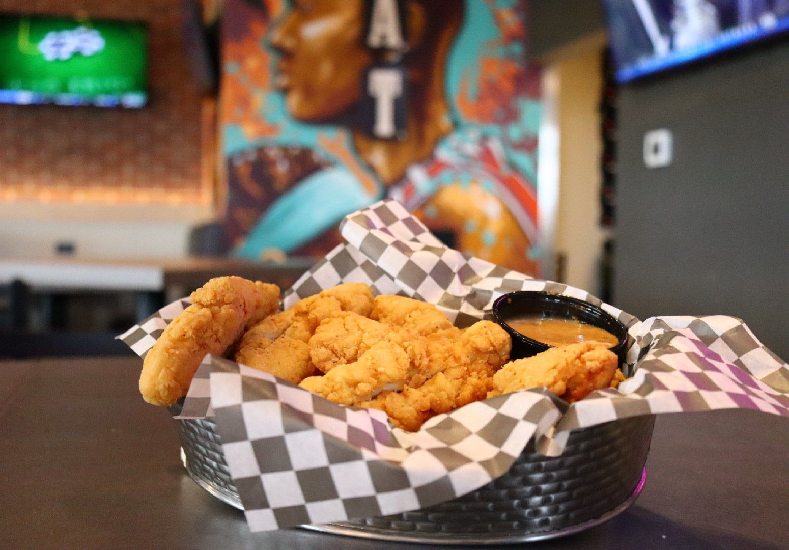 A basket of chicken strips and dipping sauce on a table.