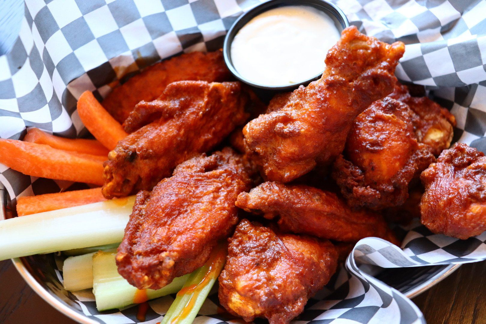 A basket of chicken wings with carrots and celery and a dipping sauce.
