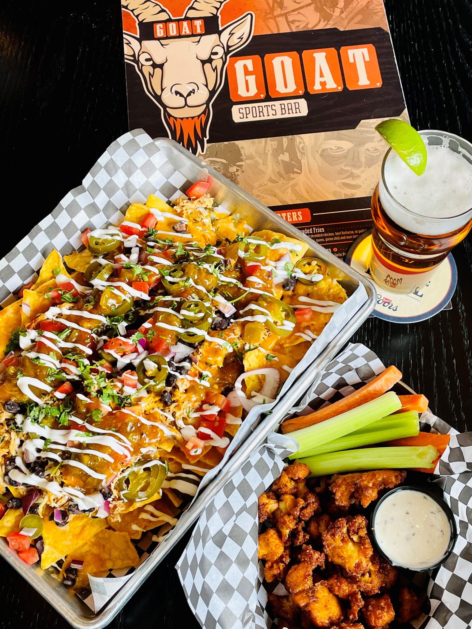 A plate of nachos , chicken wings , and a glass of beer on a table.